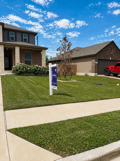 Suburban house with a blue yard sign, green lawn, concrete sidewalk, and a red truck in the driveway.