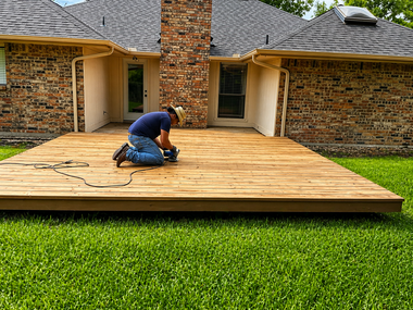 Worker installing wooden deck in front of a brick house