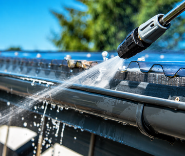 Pressure washer spraying water on a house roof gutter outdoors
