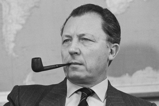 Un homme avec une pipe dans la bouche porte un costume et une cravate