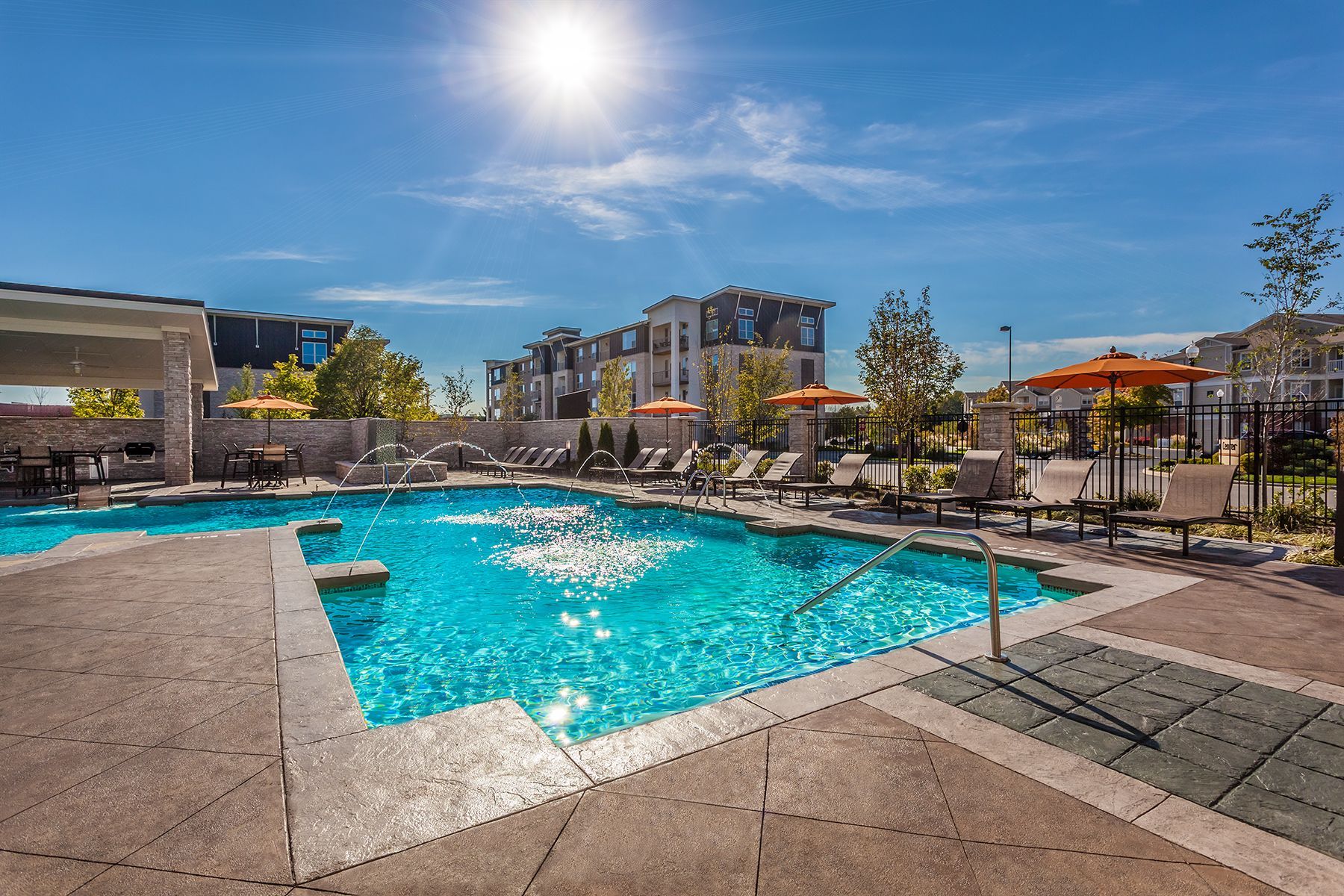 A large swimming pool surrounded by chairs and umbrellas in front of a building.
