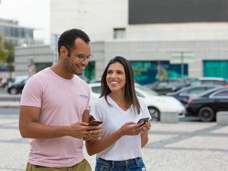 Cheerful Friends Strolling Street with smartphones - The Umbrella Insurance in Bowie, MD