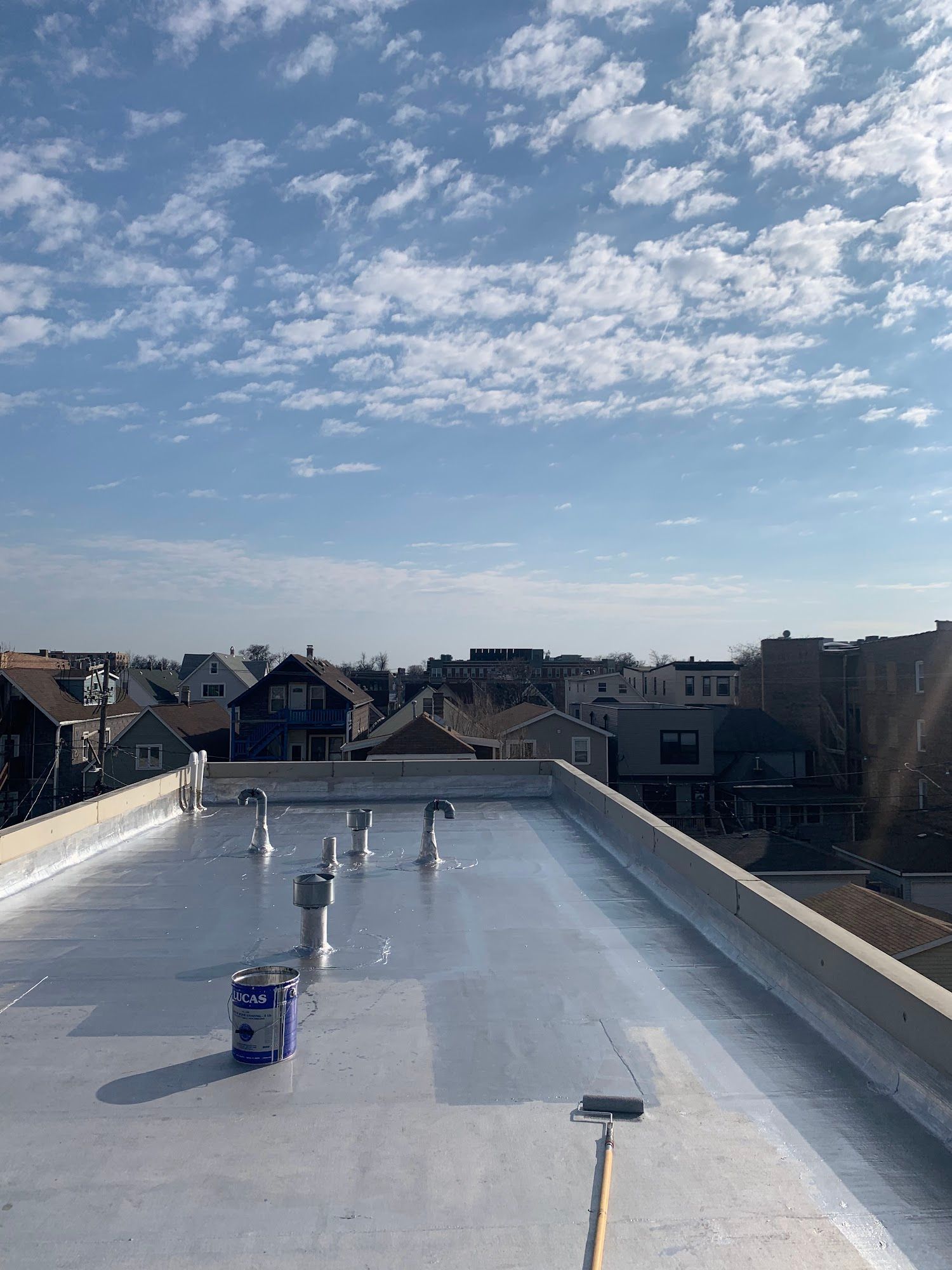 Flat rooftop under a blue, partly cloudy sky, with a few workers and houses in the distance.