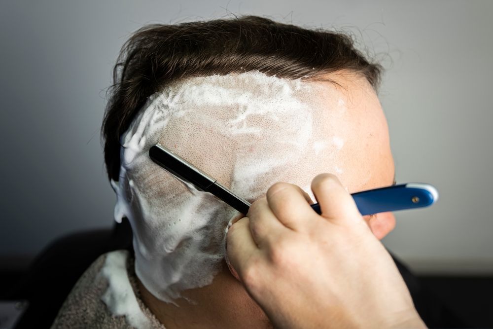 A man is shaving his head with a razor.