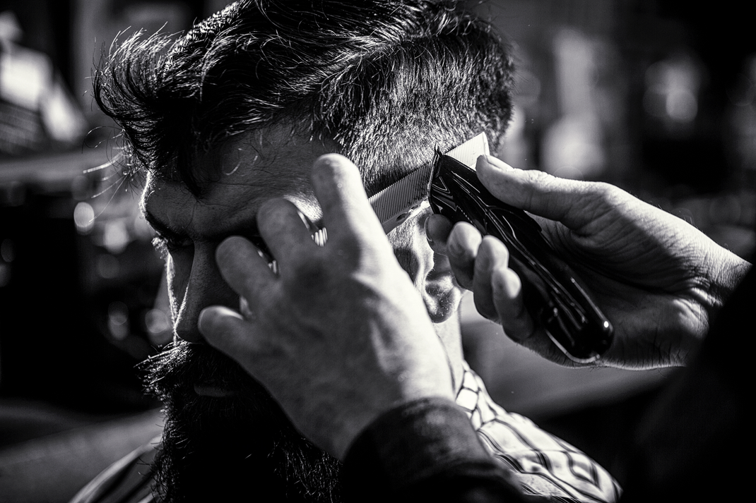 A man is getting his hair cut by a barber in a black and white photo.