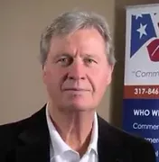 A man in a suit and white shirt is standing in front of a sign.
