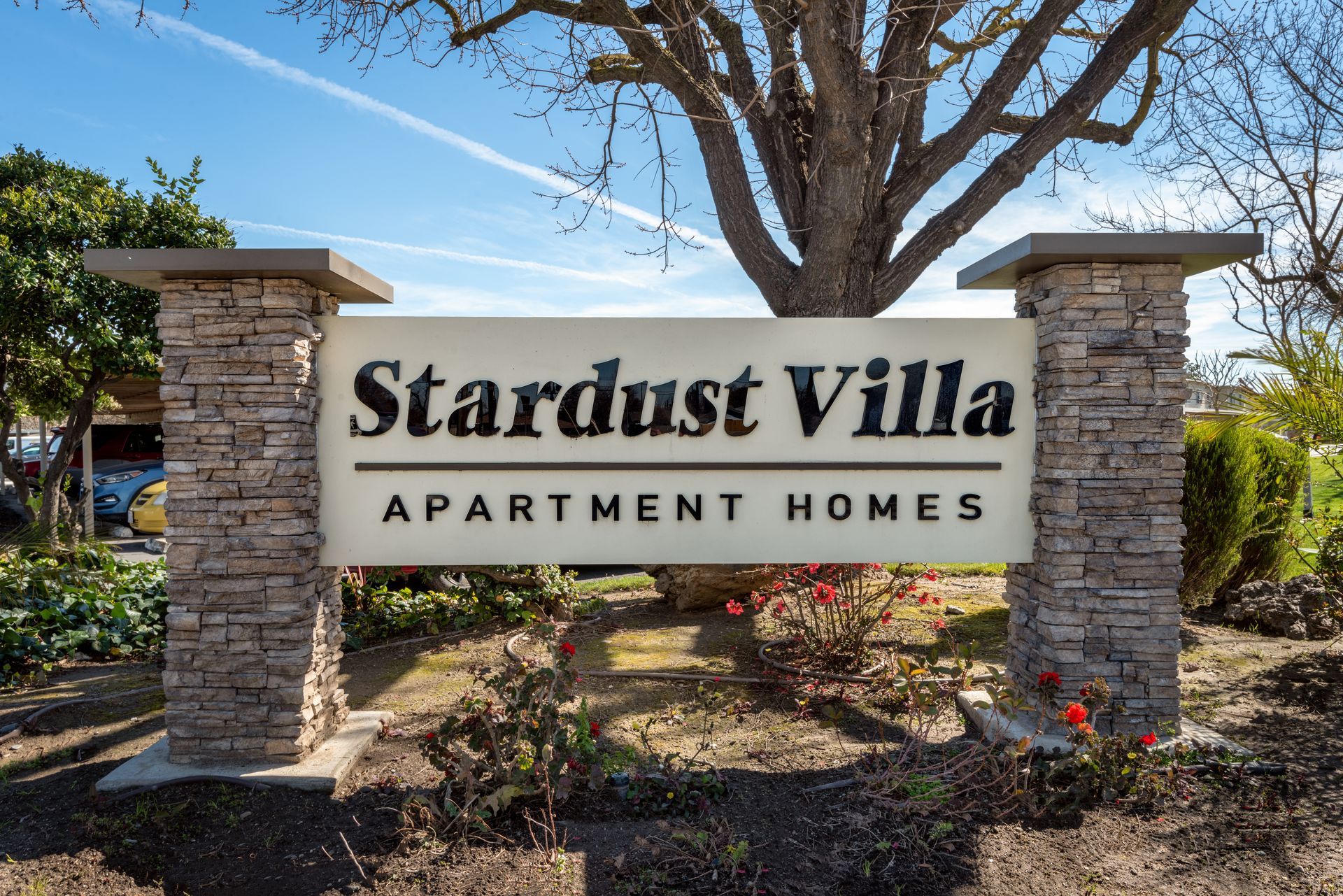 Stardust Villa apartment sign with text on a white background, stone pillars, blue sky.