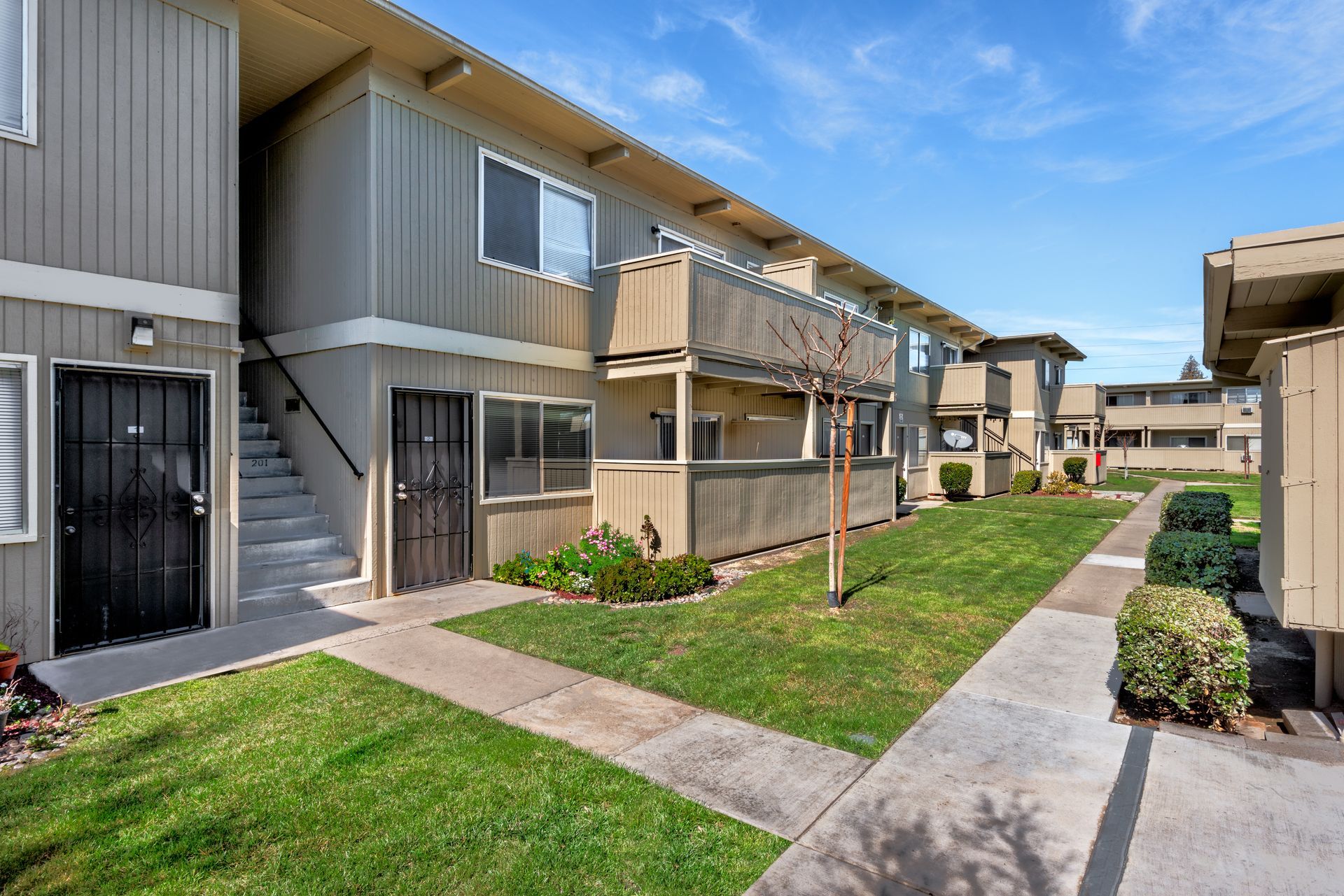 Apartment building with beige siding, green grass, and a blue sky.