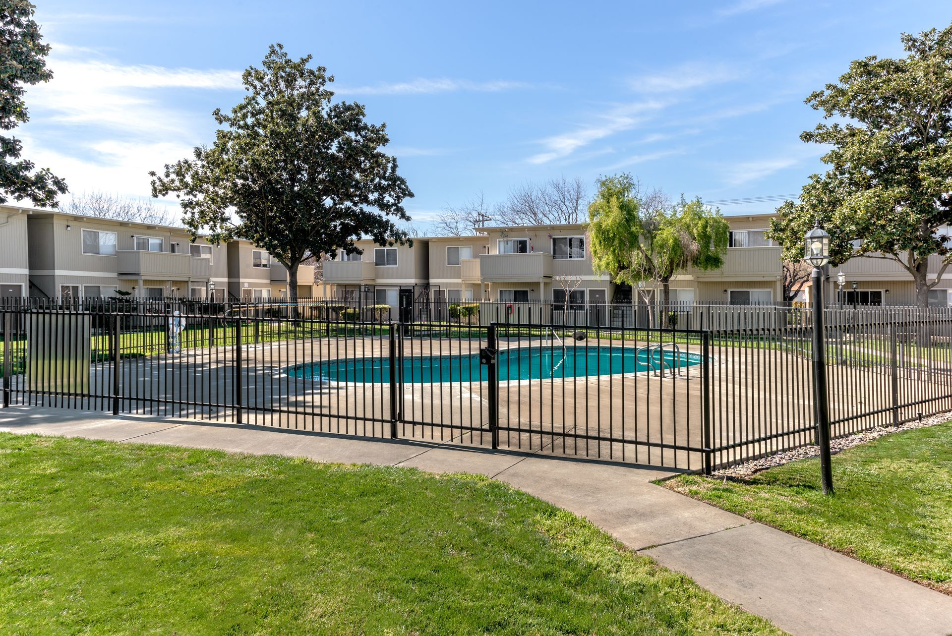 Townhouses with a fenced pool and green lawn under a blue sky.