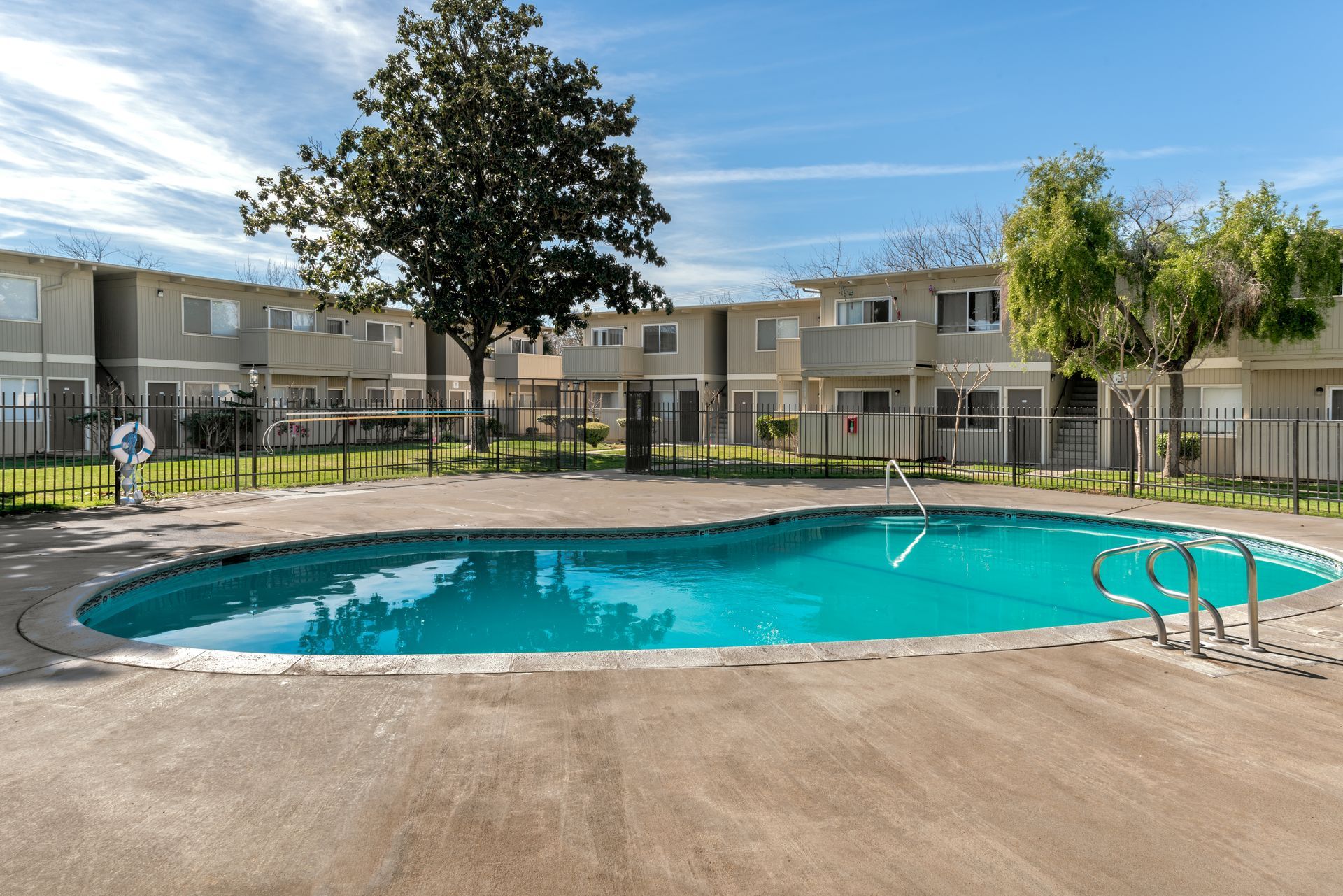 Apartment complex with a turquoise pool, trees, and a sunny sky.