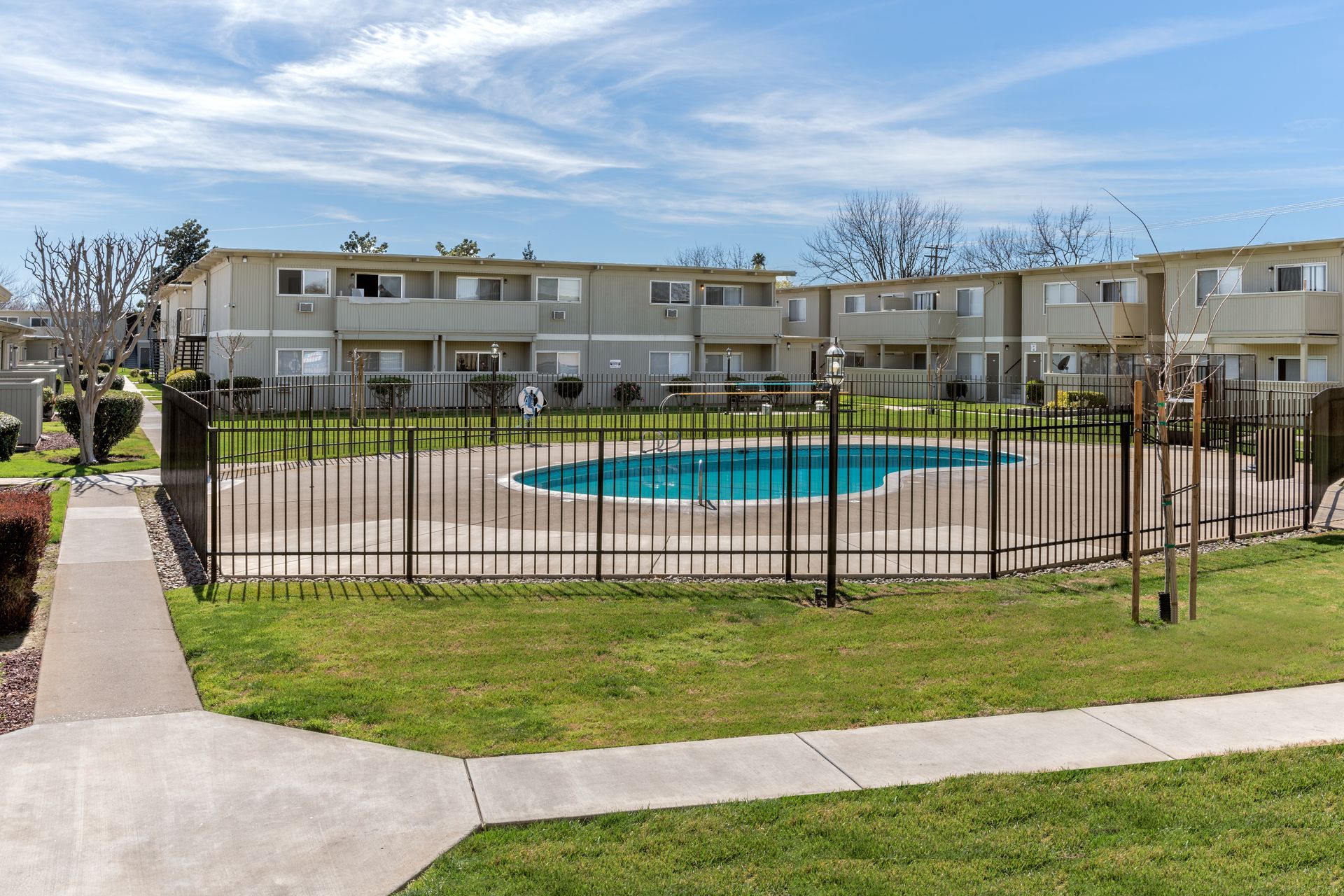 Apartment complex with a fenced pool and walkway under a cloudy sky.