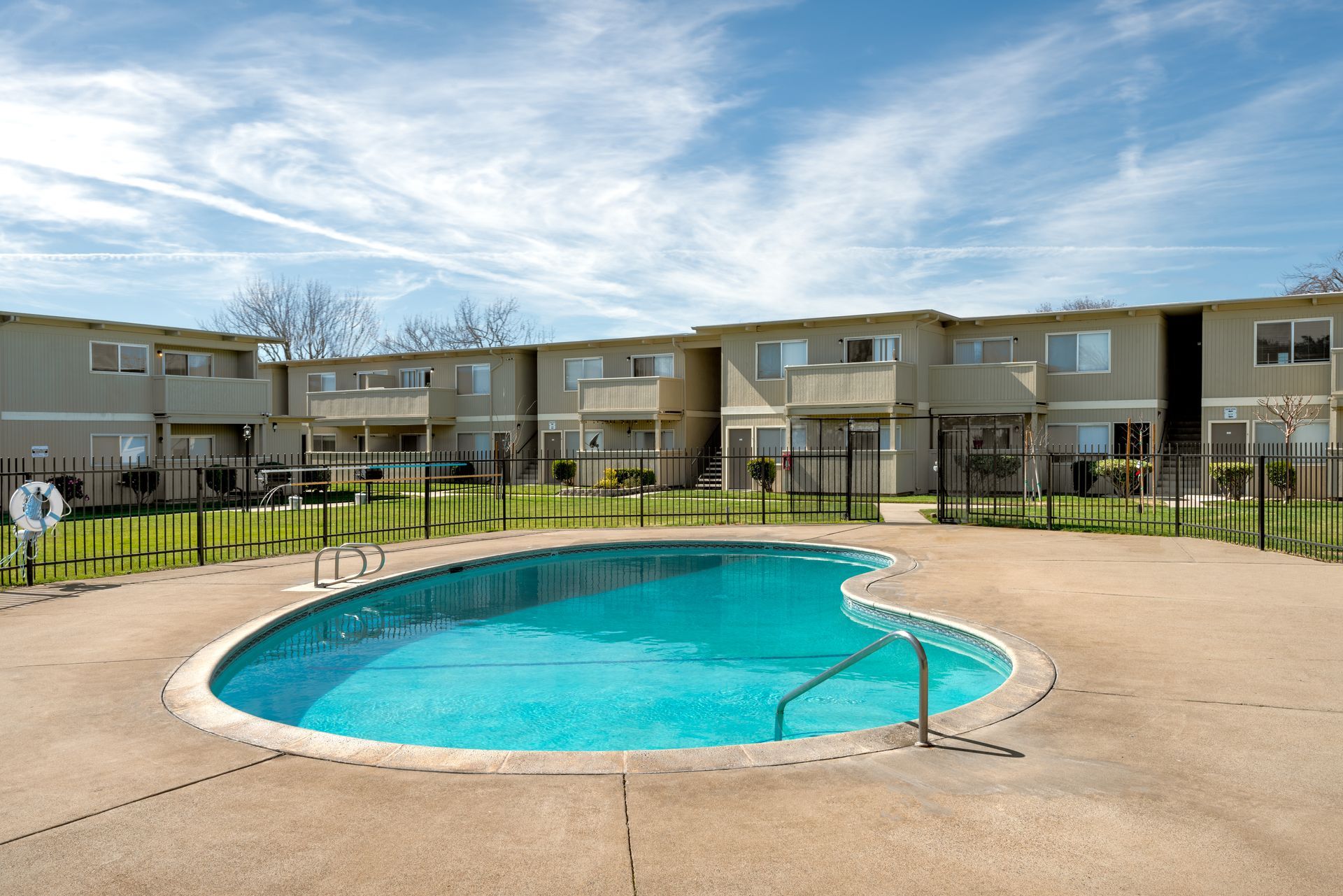 Swimming pool in front of a two-story apartment building on a sunny day.
