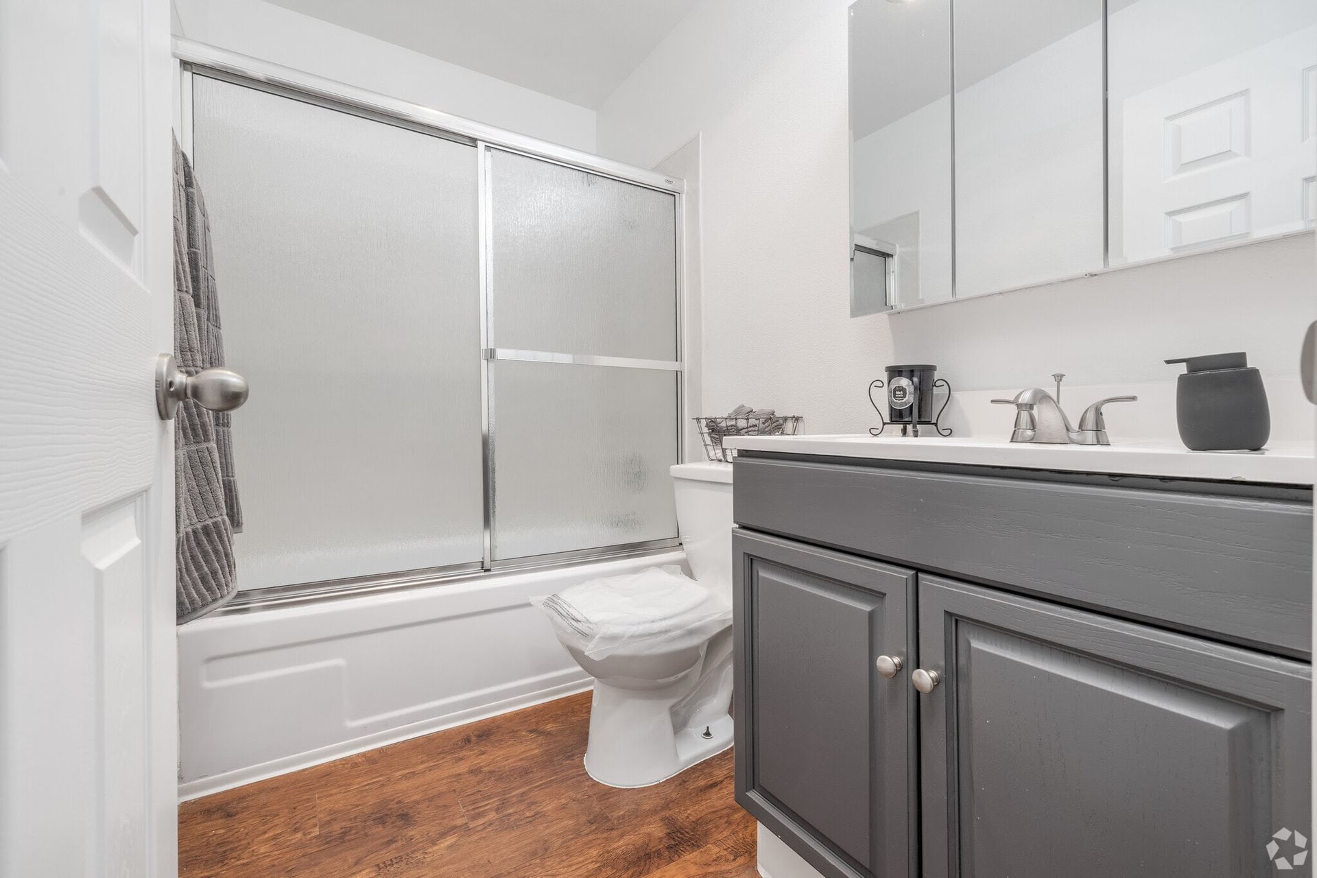 Bathroom with a white toilet, gray vanity, shower with frosted glass door, and dark wood-look flooring.