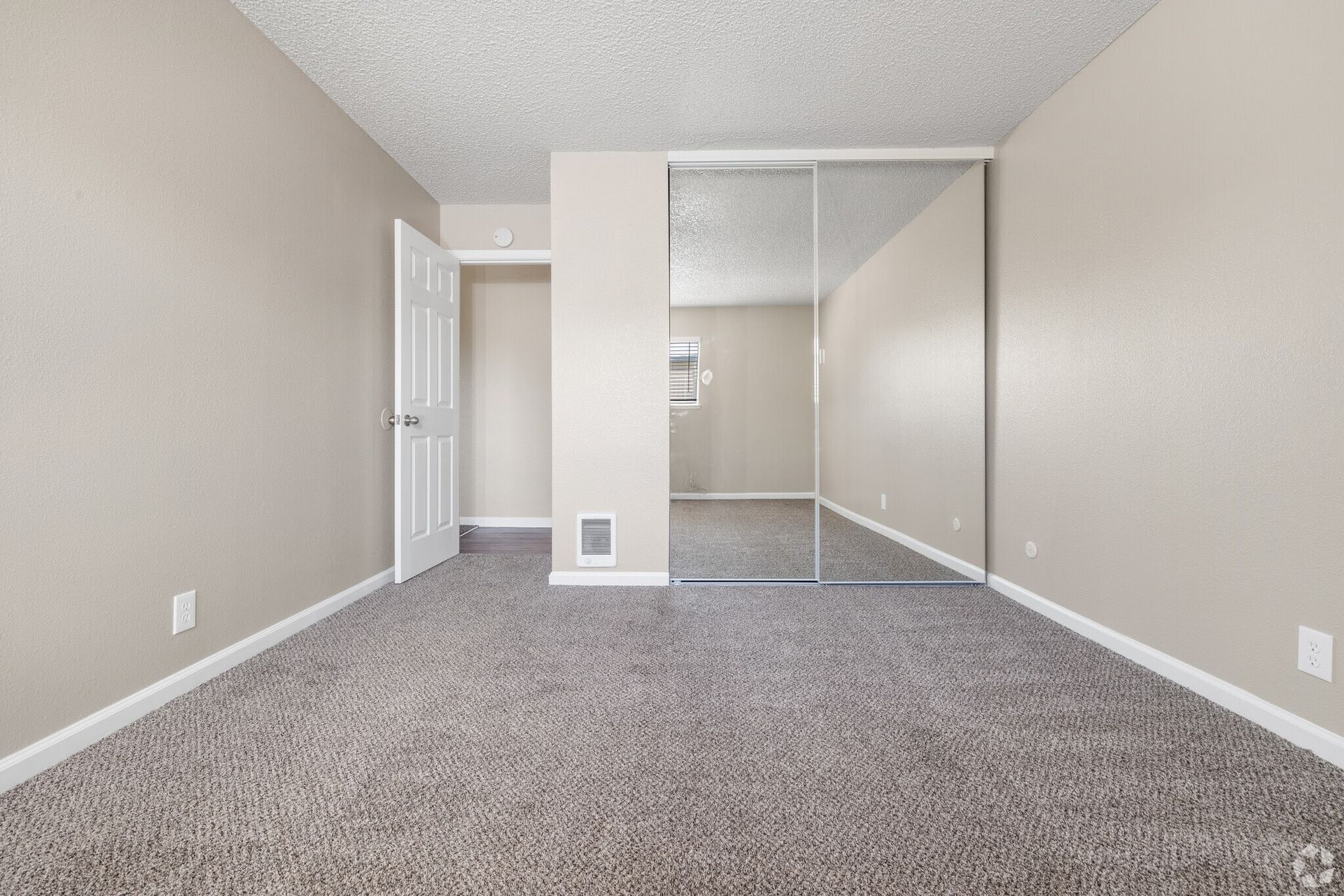 Empty bedroom with beige walls, carpet, and mirrored closet. Doorway visible.