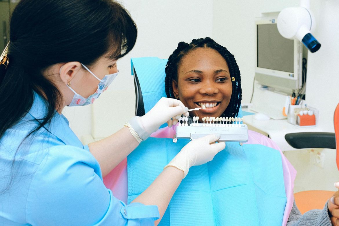 A woman is sitting in a dental chair looking at her teeth in a mirror.