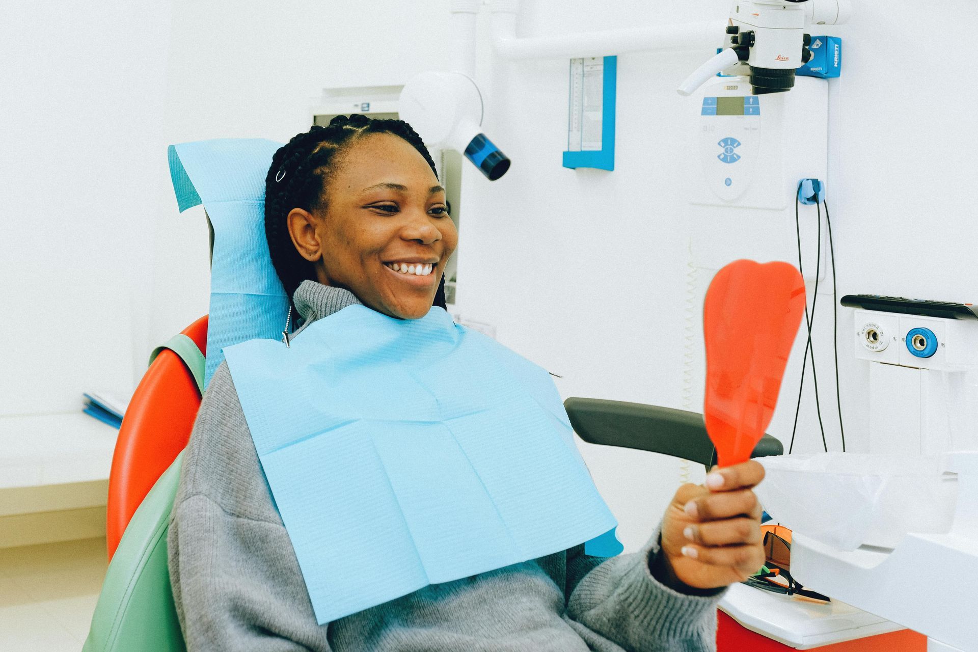 A woman is sitting in a dental chair holding a mirror and smiling.