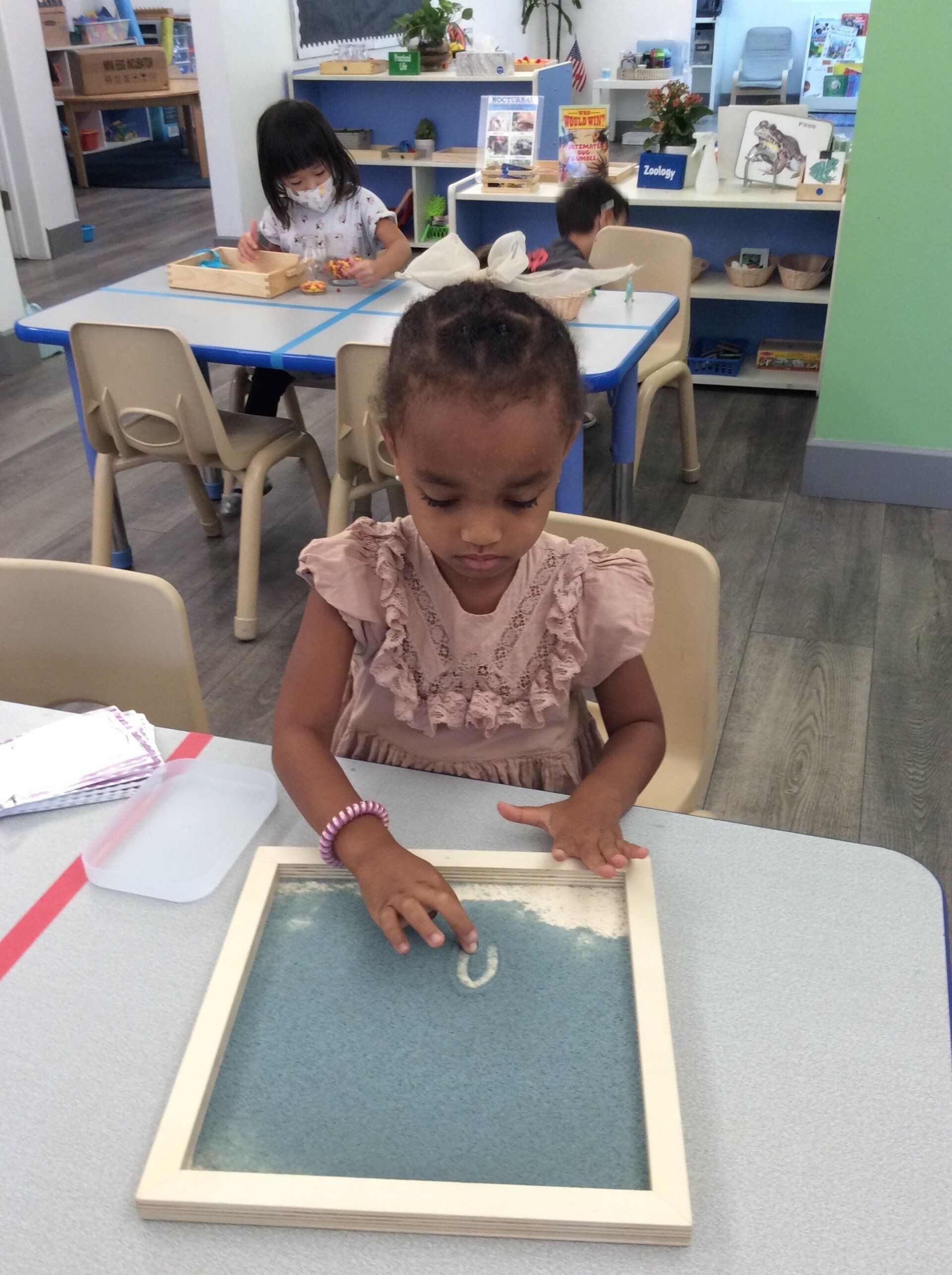 Child tracing letters on a Montessori writing tray