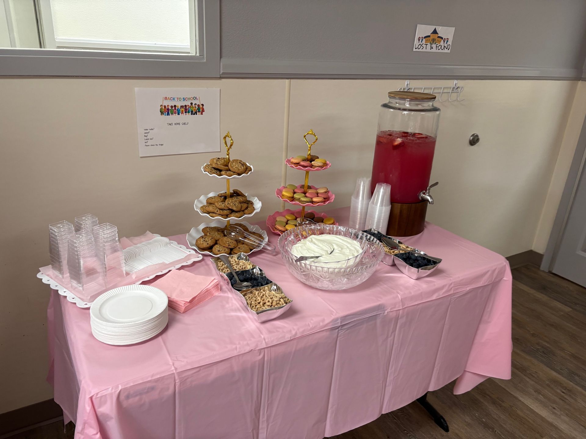 A table with a pink tablecloth and plates of food and drinks on it.