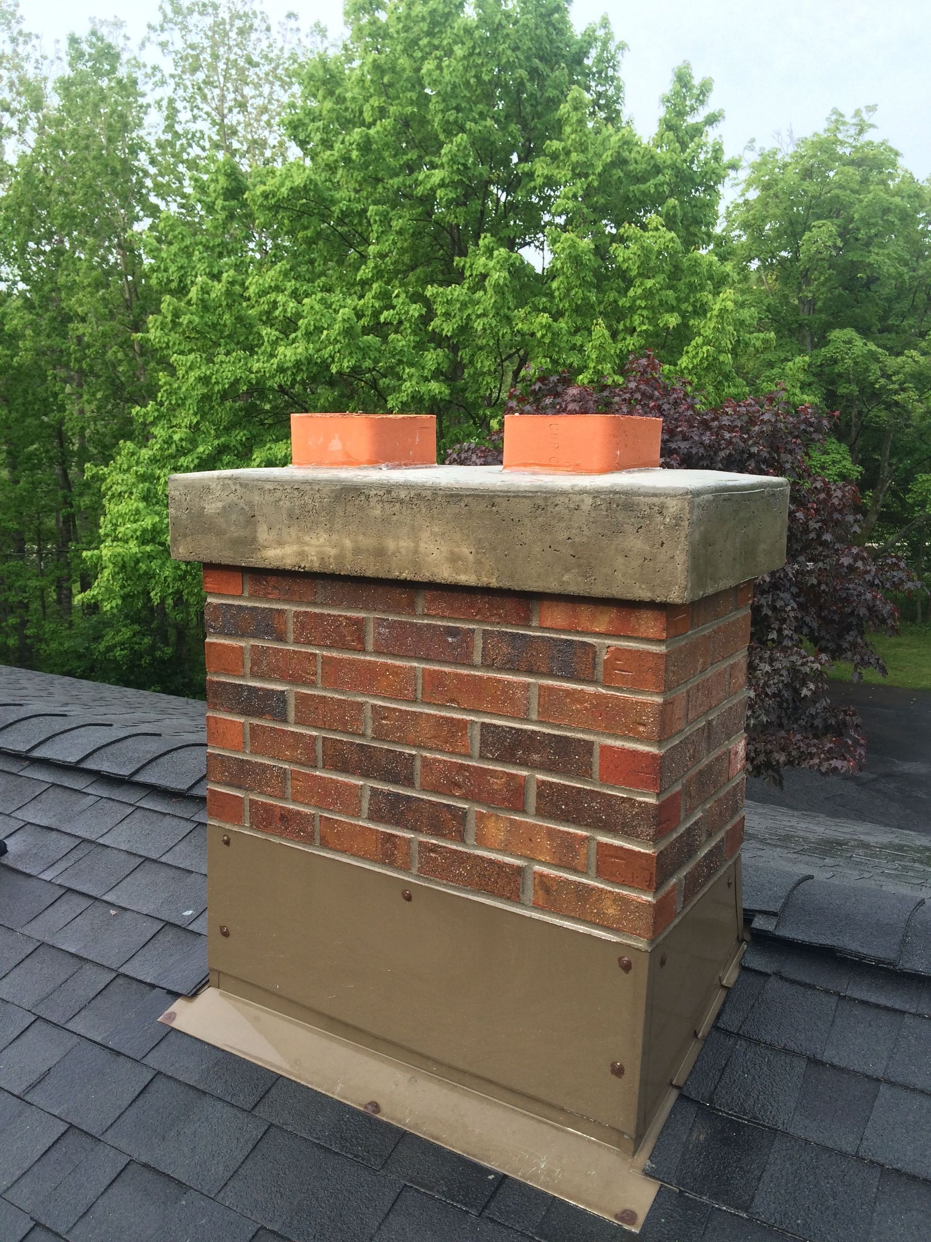 Person on ladder near a house roof, wearing work belt and hoodie, near a brick chimney.