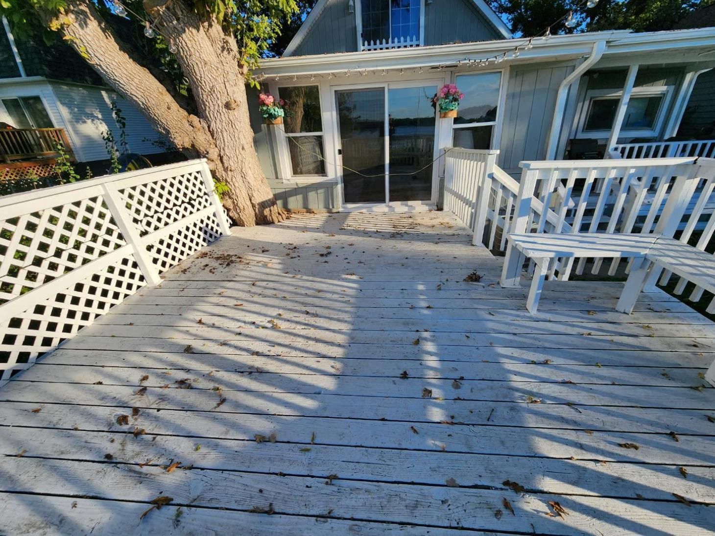 A white deck with a bench and chairs in front of a house.