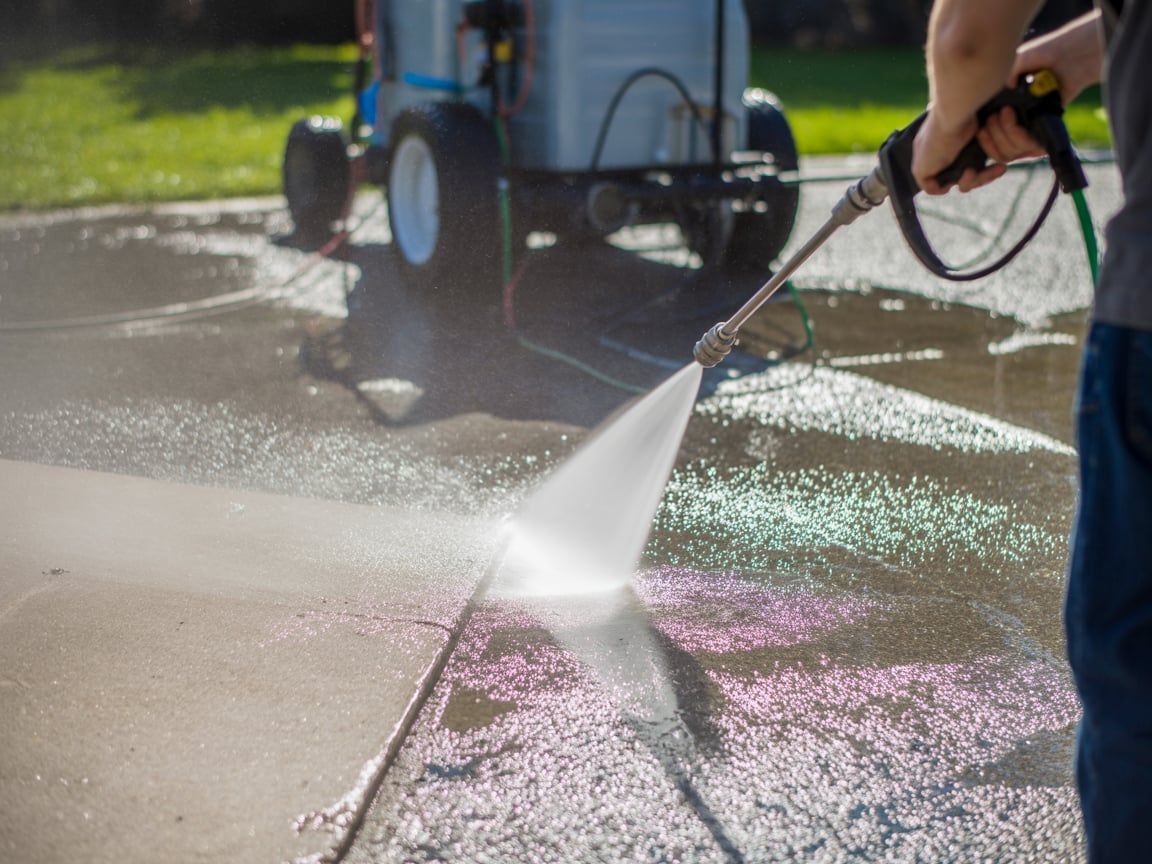 Person pressure washing a concrete surface with visible water spray.