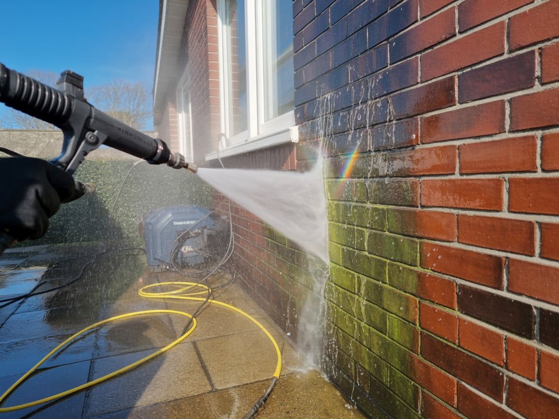 Power washer spraying a brick wall, cleaning away green algae.