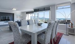 Bright dining room with glass table, patterned chairs, red rug, and ocean view through large windows
