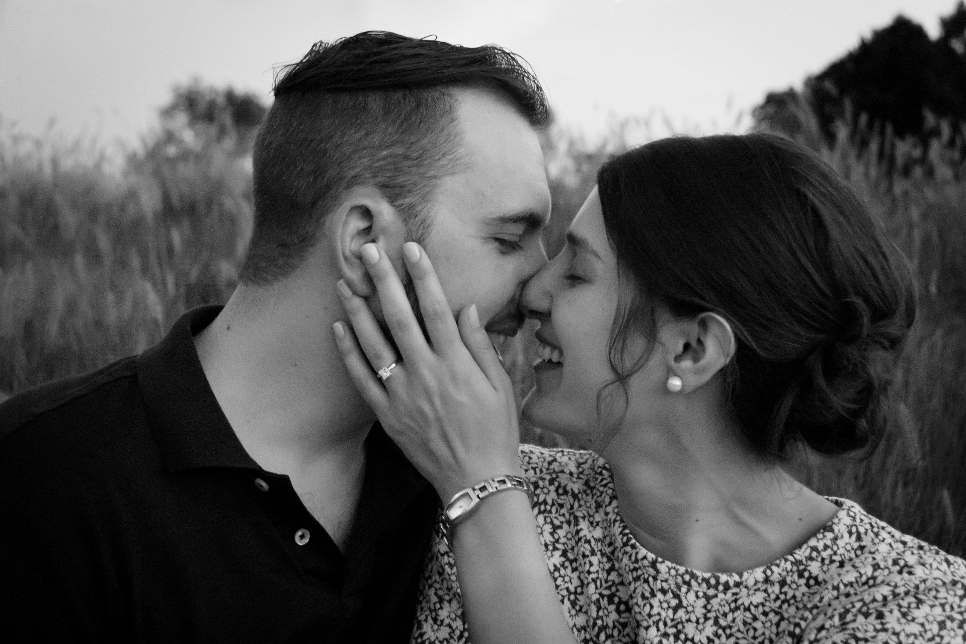 A man and a woman are kissing in a field in a black and white photo.