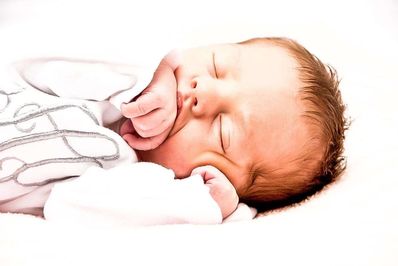 A newborn baby is sleeping on a white blanket.