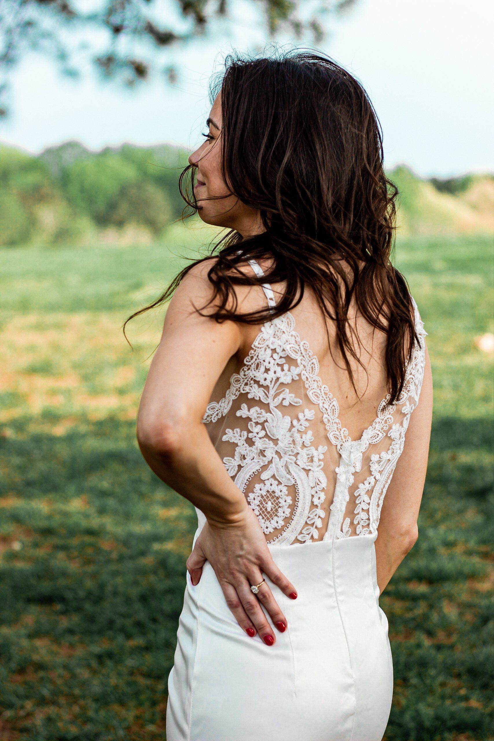 A woman in a white wedding dress is standing in a field.