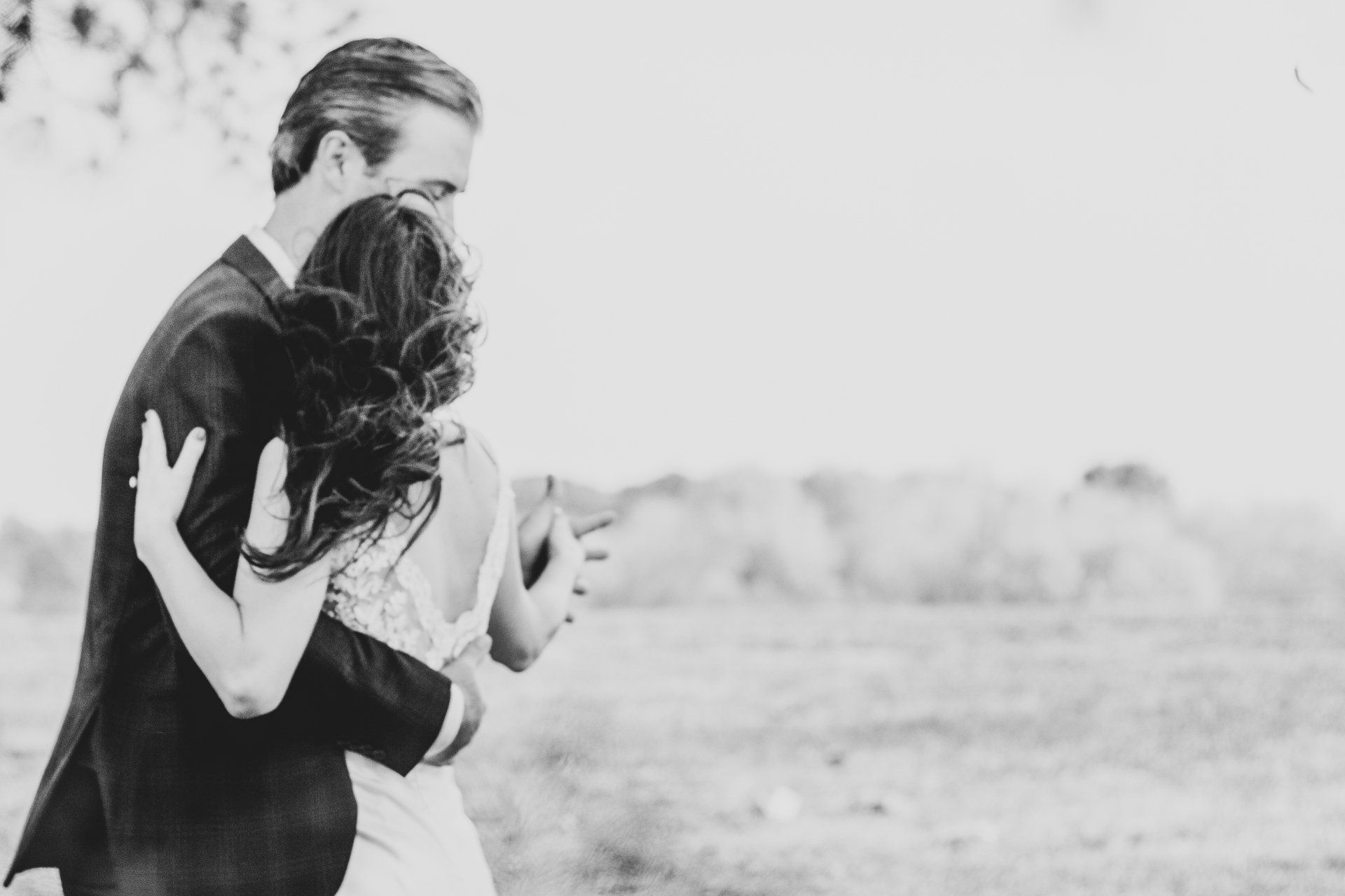 A black and white photo of a bride and groom hugging in a field.