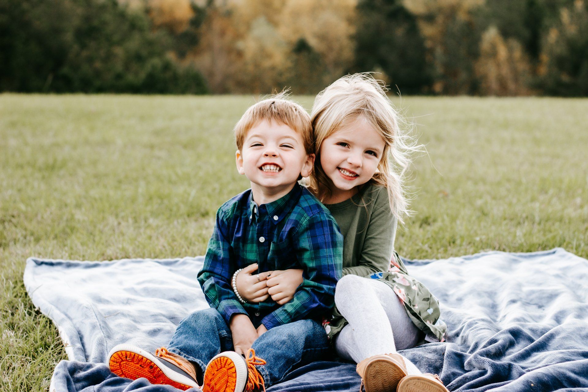 A boy and a girl are sitting on a blanket in a field.