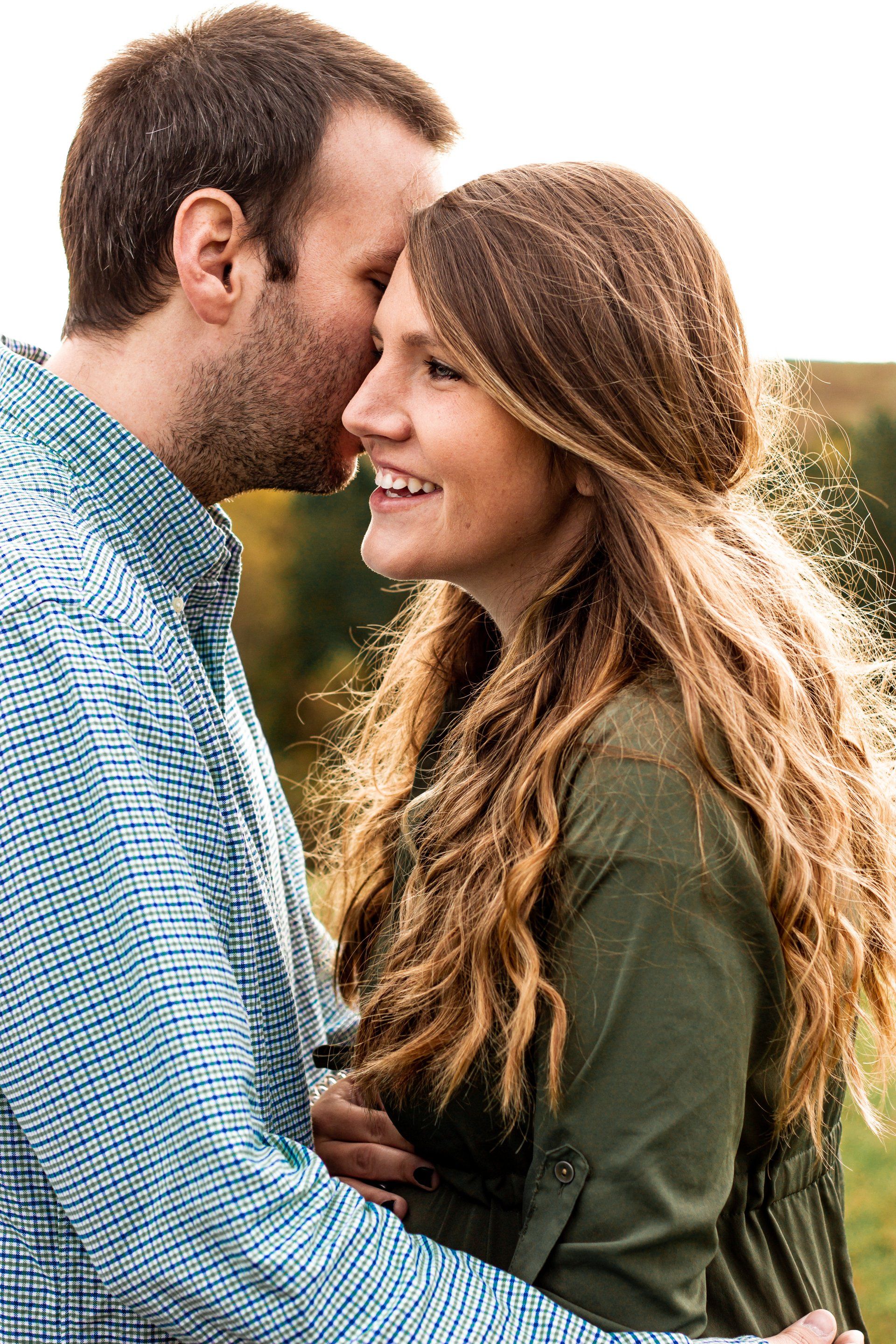A man is kissing a woman on the forehead in a field.
