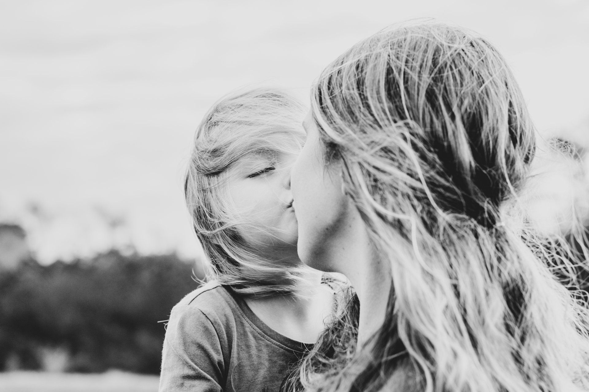 A mother and daughter are kissing in a black and white photo.