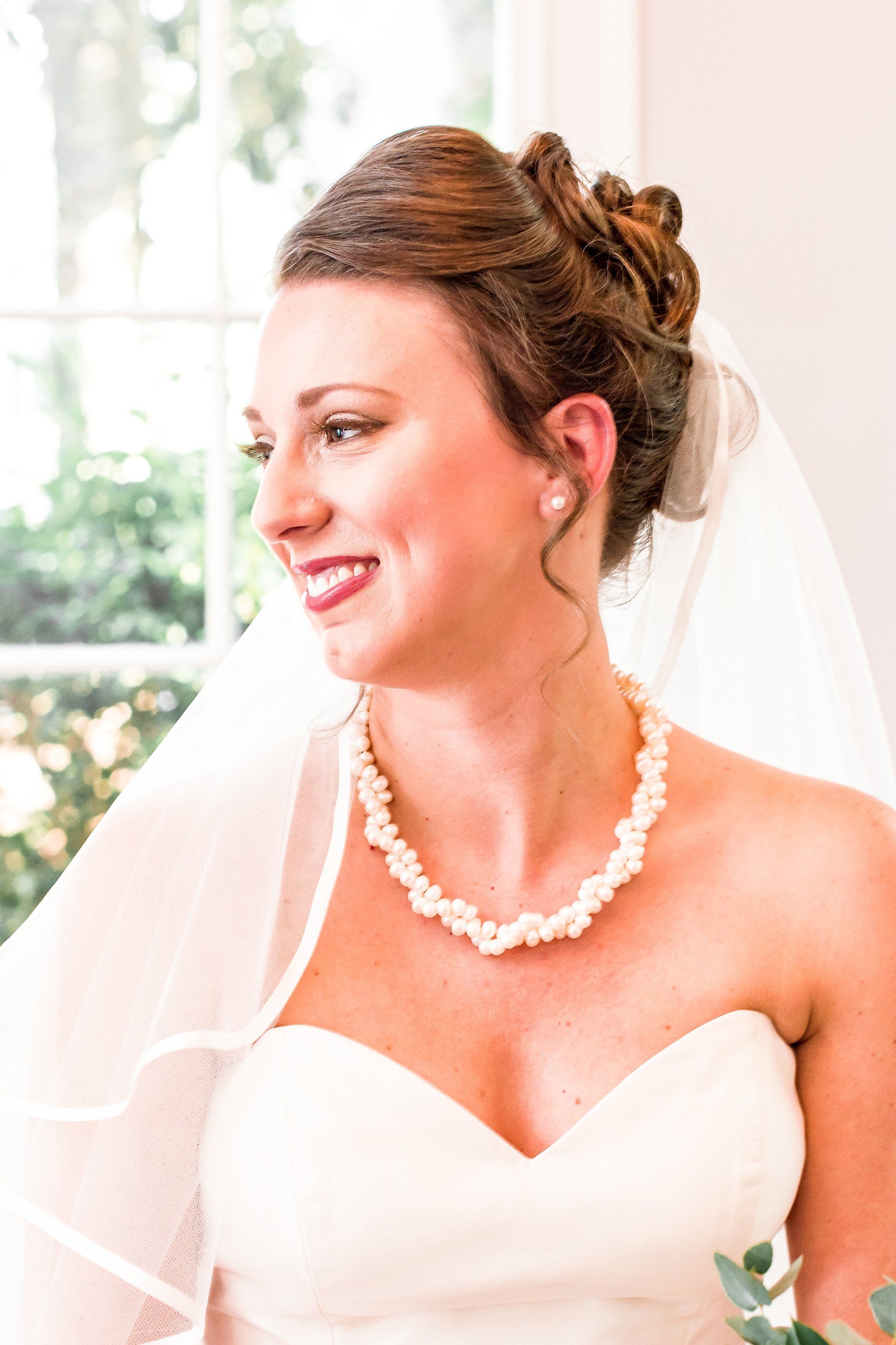 The bride is wearing a pearl necklace and a veil.