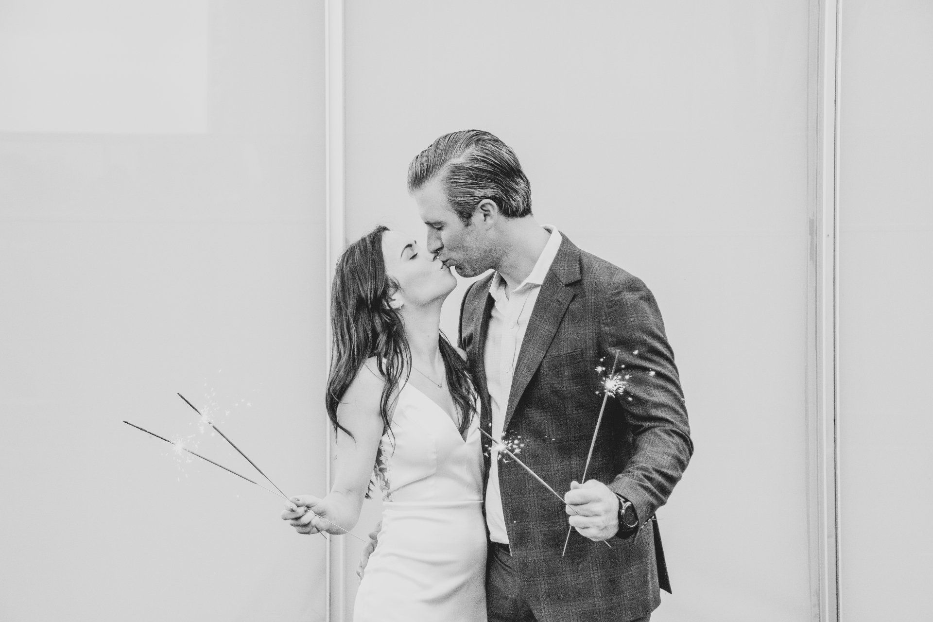 A bride and groom kissing while holding sparklers in a black and white photo.