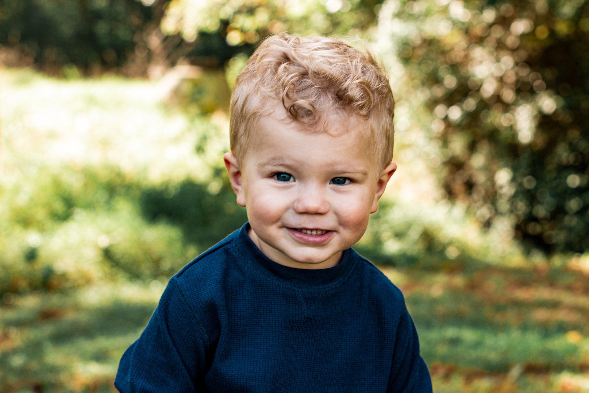 A little boy in a blue sweater is smiling for the camera.