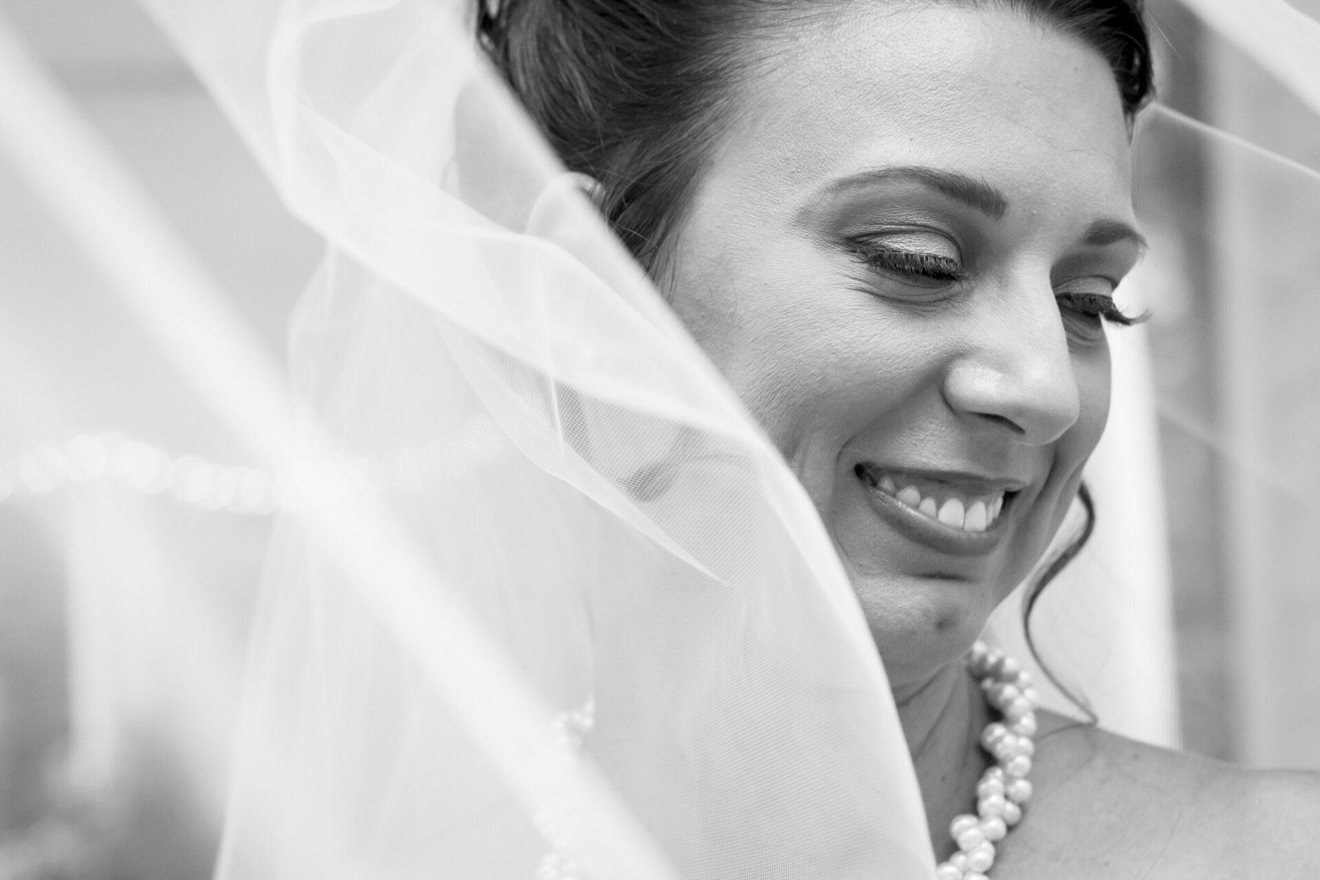 A black and white photo of a bride with her veil blowing in the wind.