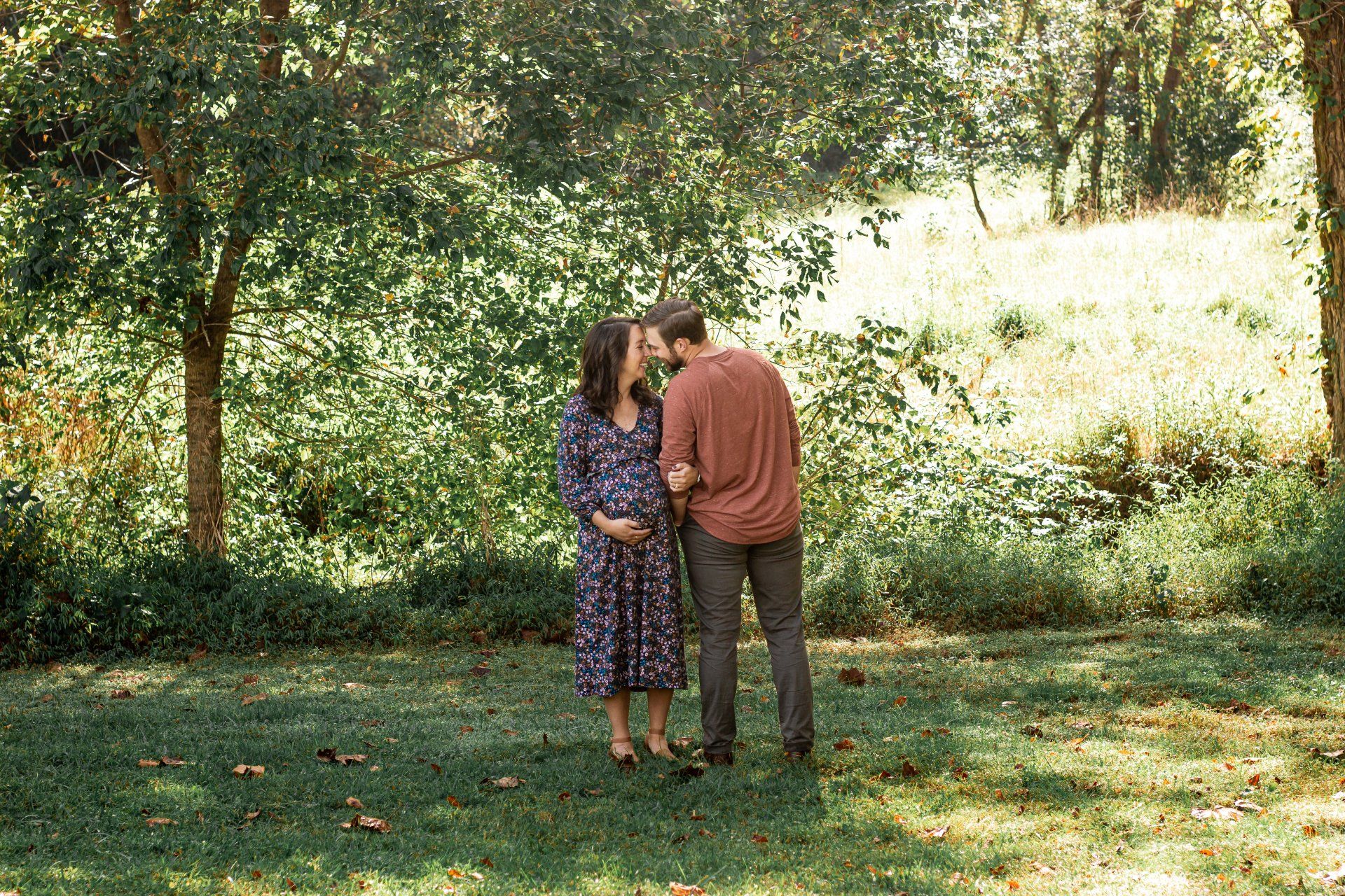 A man and a pregnant woman are kissing in a park.