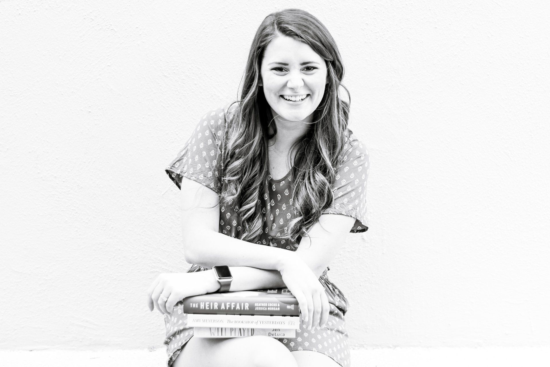 A woman is sitting on the floor holding a stack of books.