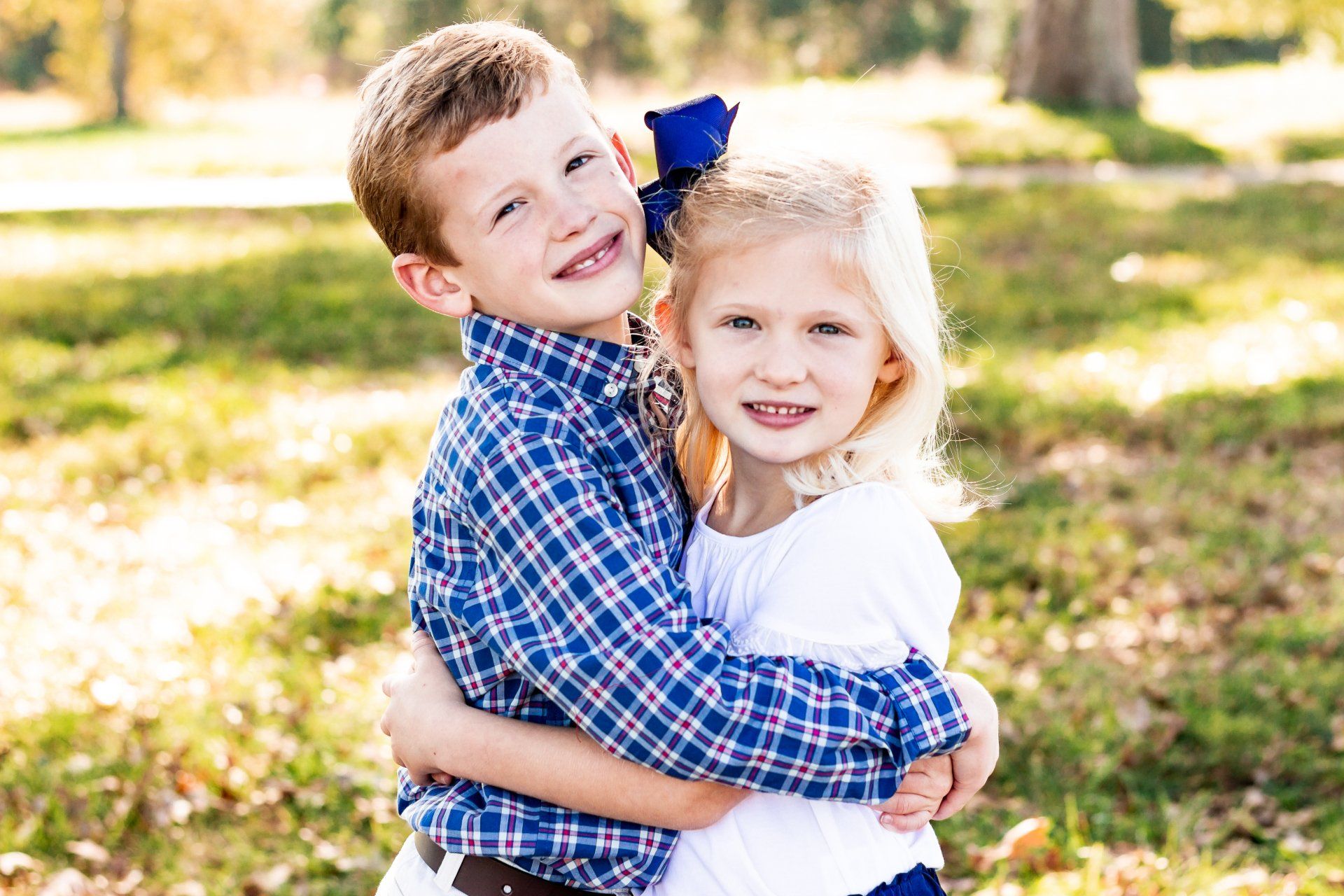 A boy and a girl are hugging each other in a park.