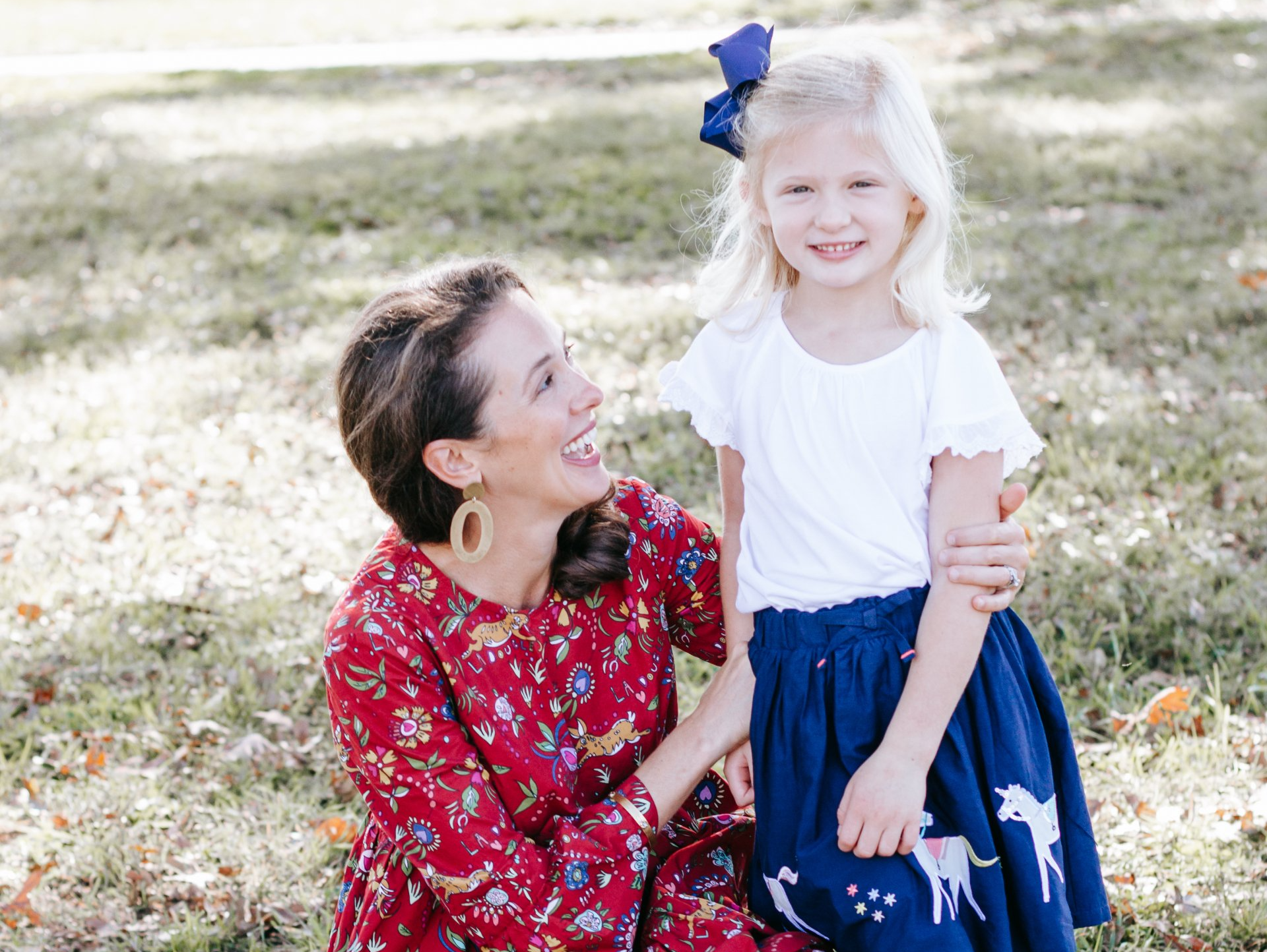 A woman is kneeling down next to a little girl in a blue skirt.