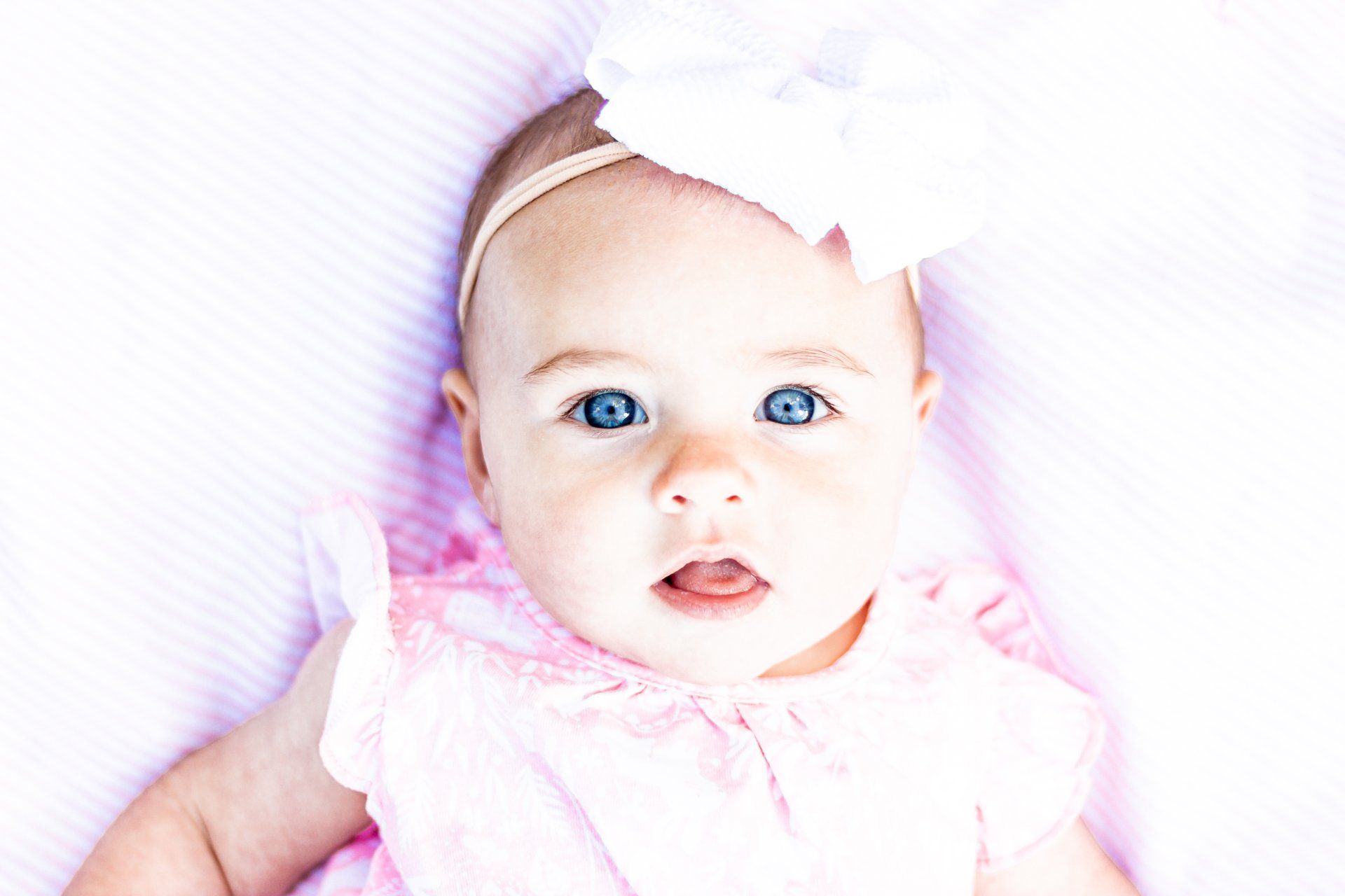 The baby is wearing a pink dress and a white headband.