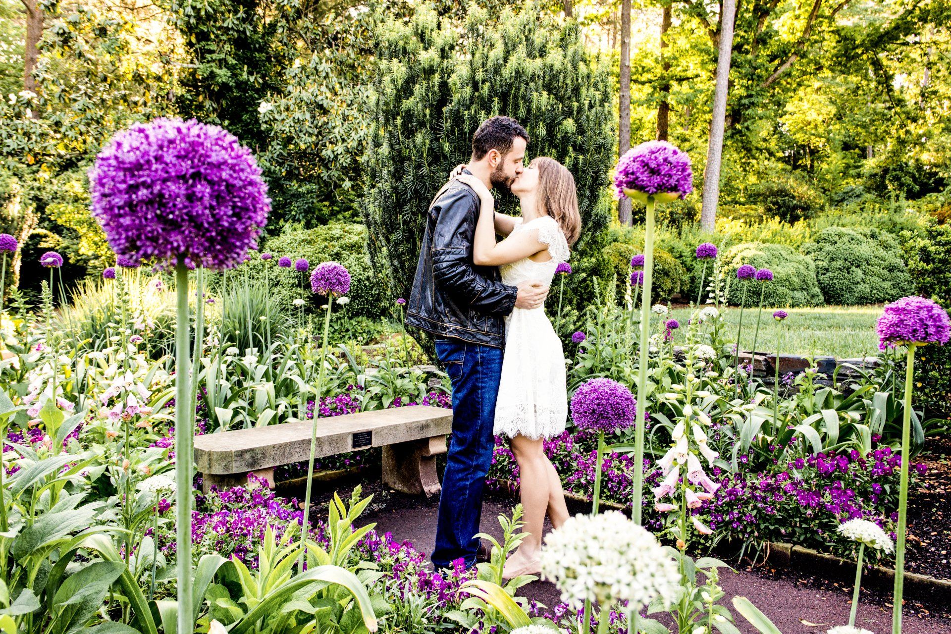 A man and a woman are kissing in a garden surrounded by purple flowers.