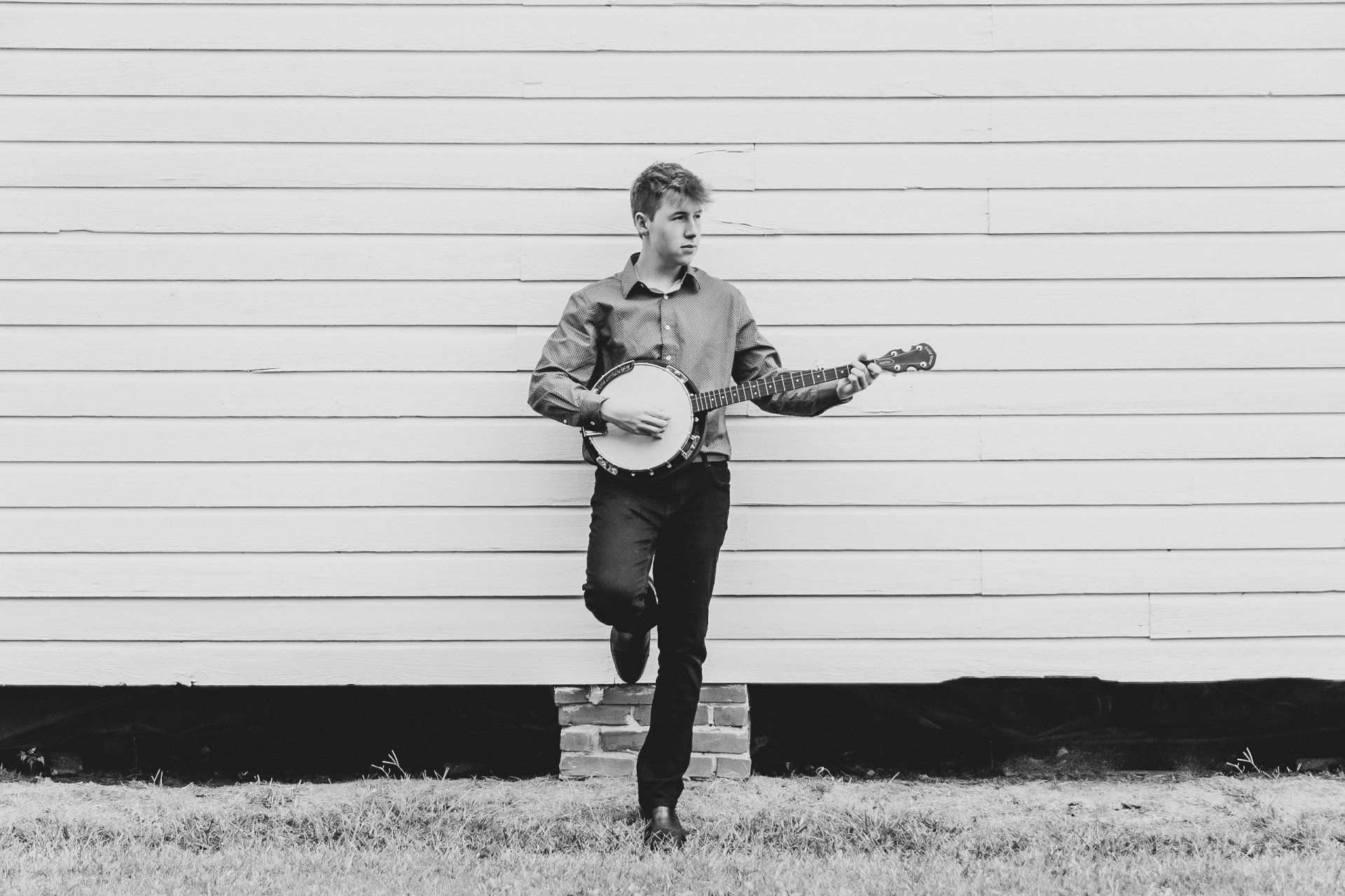 A man is playing a banjo in front of a white wall.