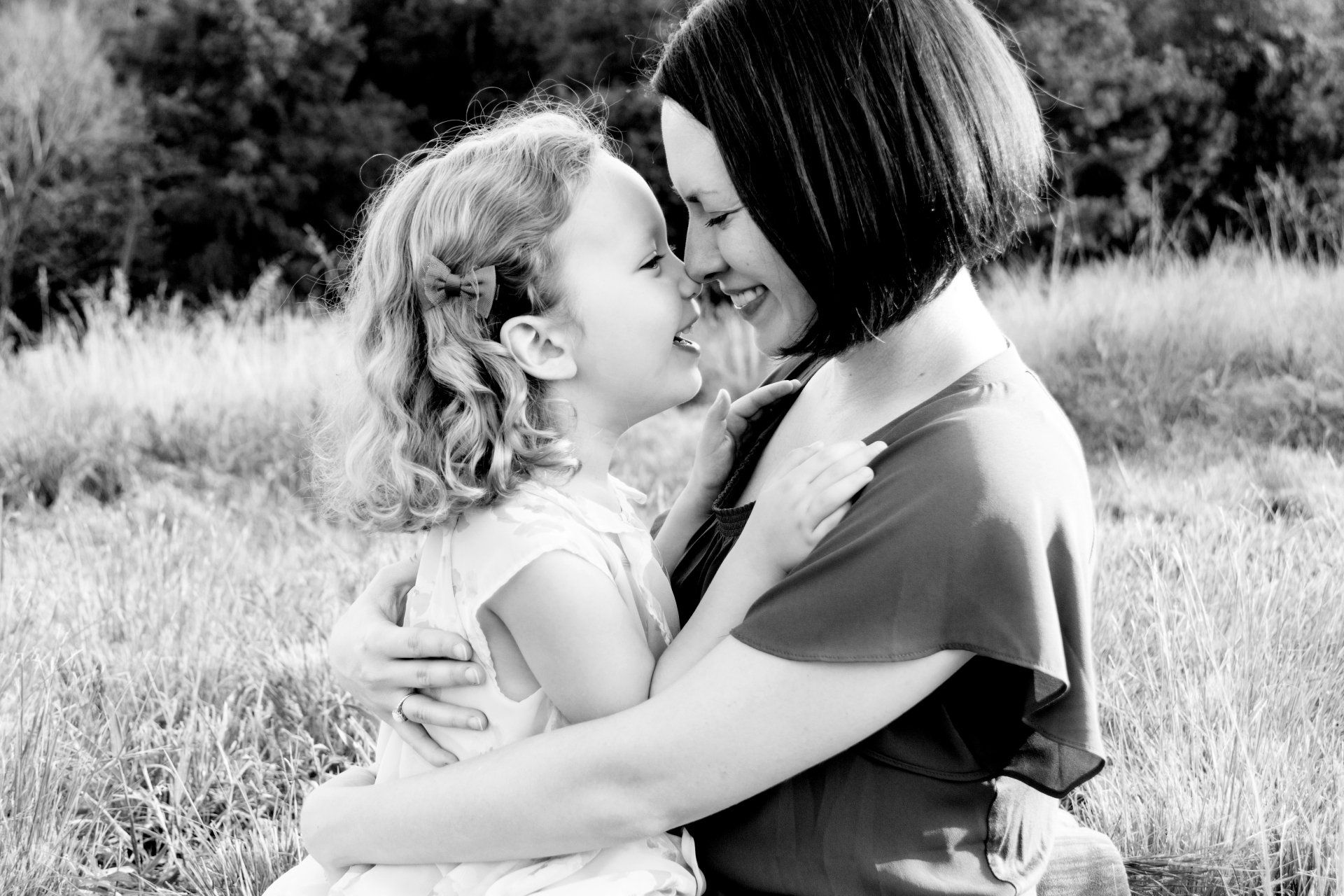 A black and white photo of a woman and a little girl hugging each other in a field.