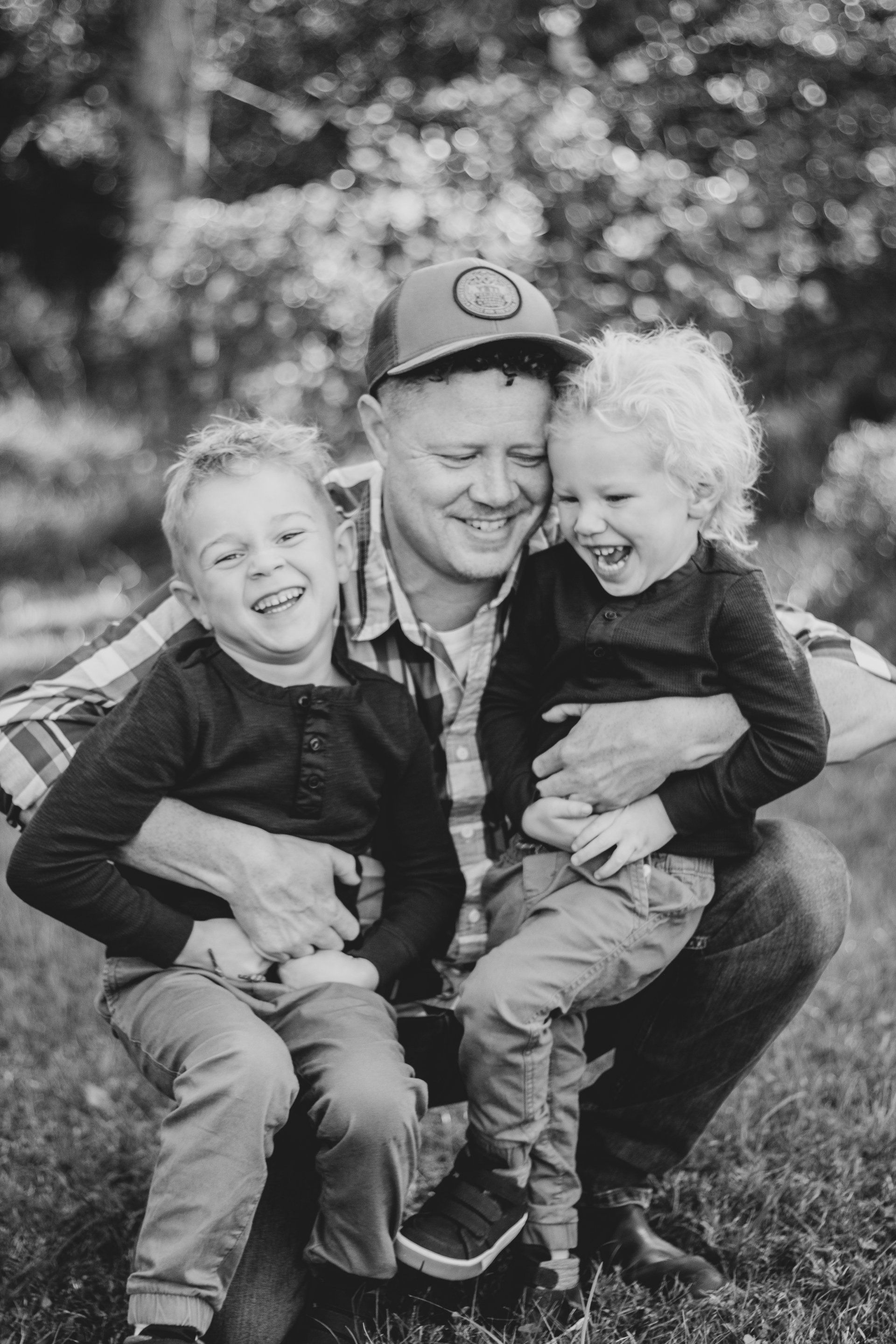 A man is kneeling down with two young boys in his arms.
