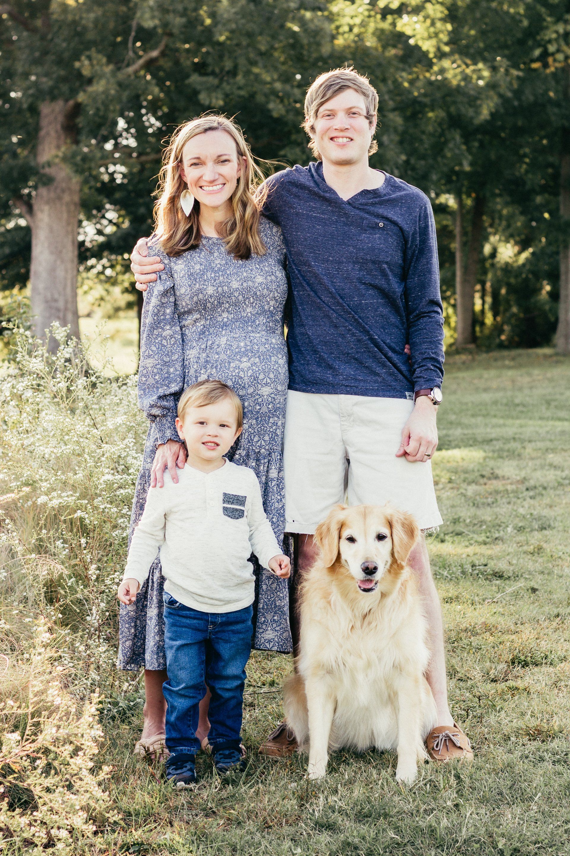A family posing for a picture with a dog in the grass.