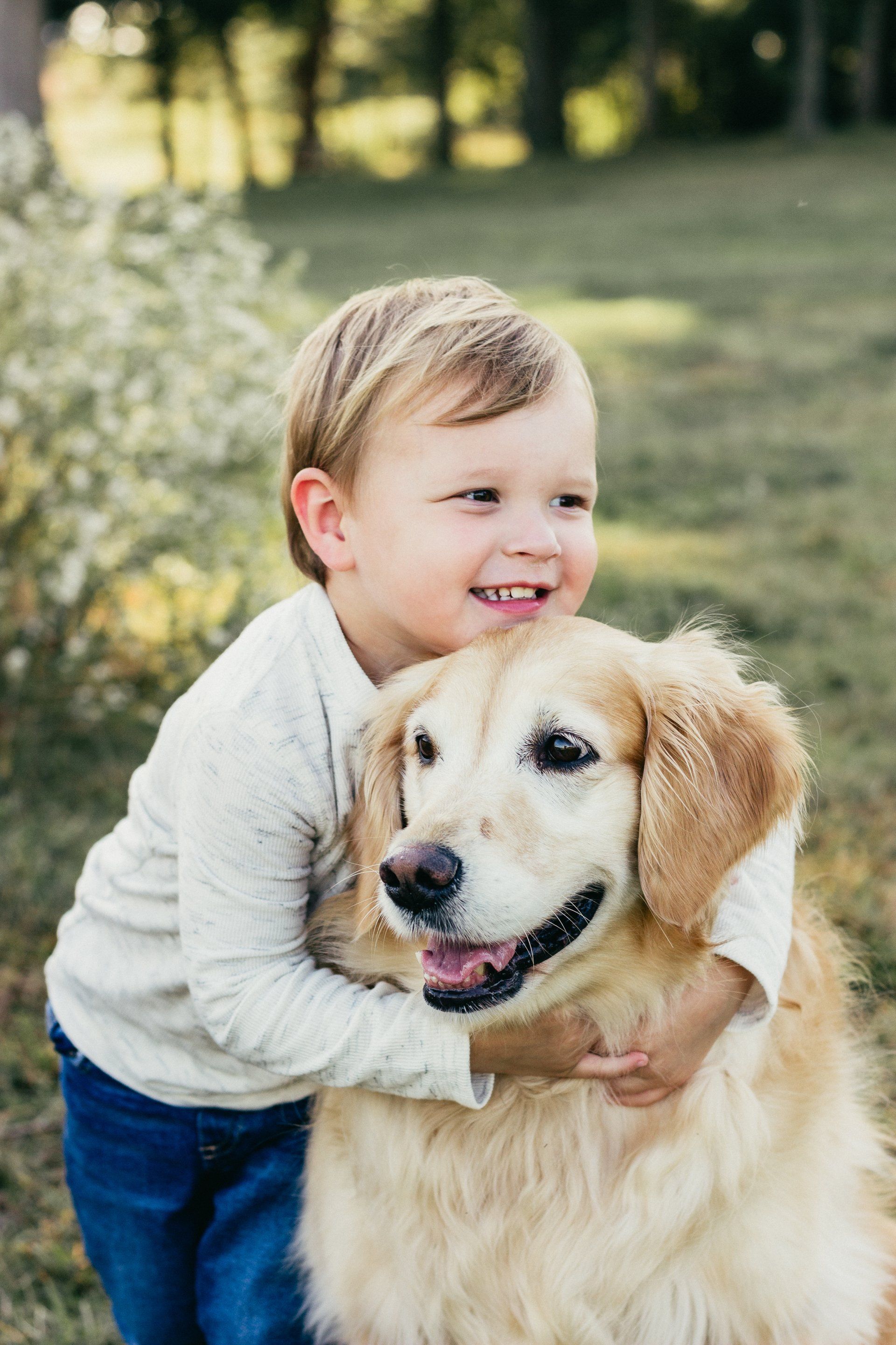 A little boy is hugging a golden retriever dog in a park.