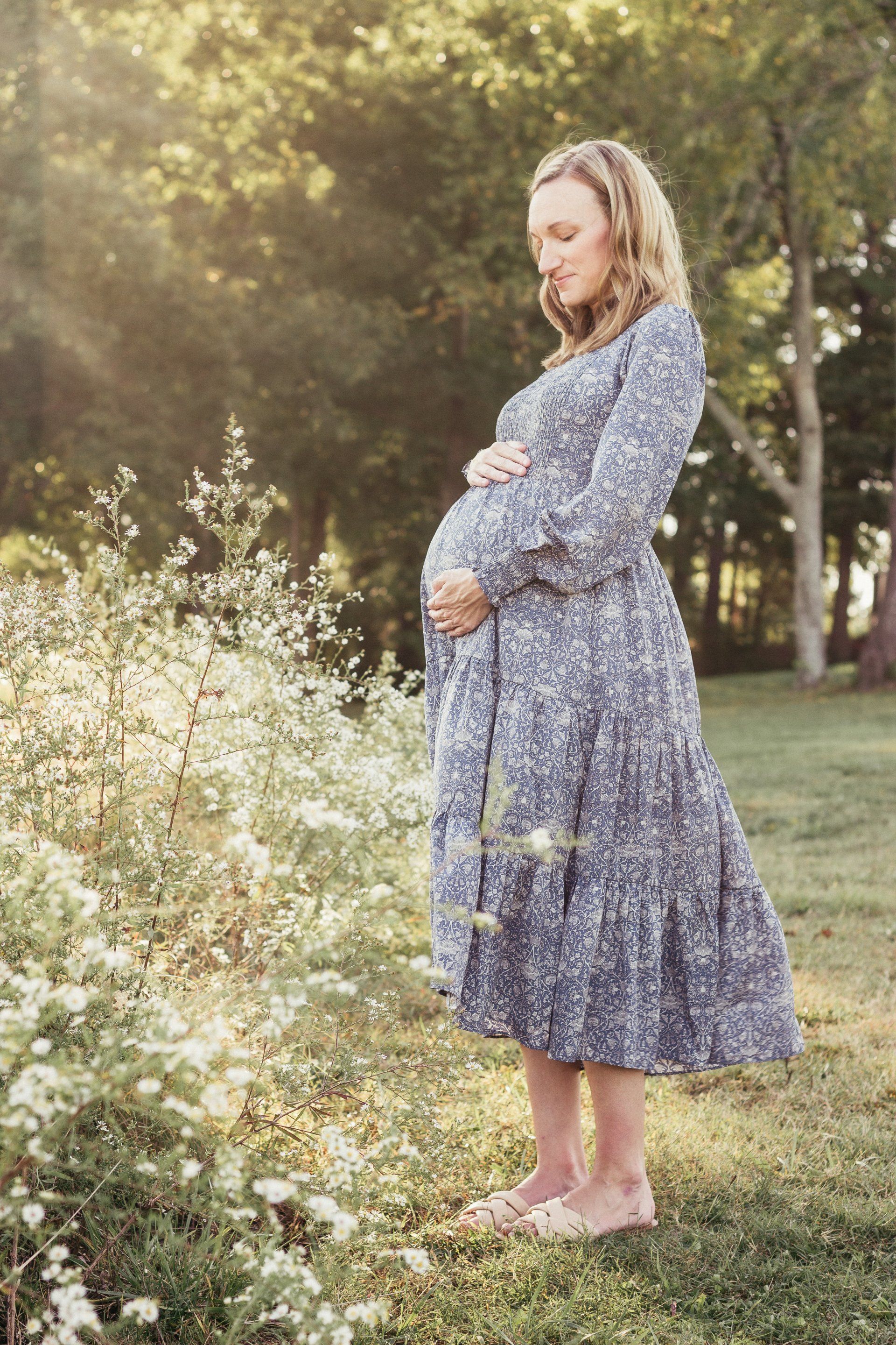 A pregnant woman in a blue dress is standing in a field of flowers.
